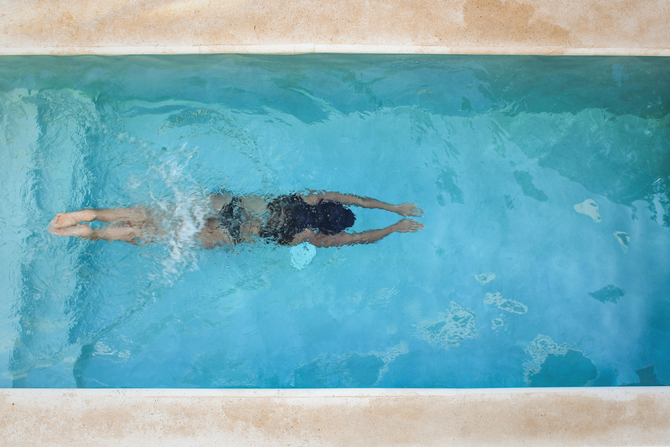 Person swimming freestyle in a blue pool, viewed from above.