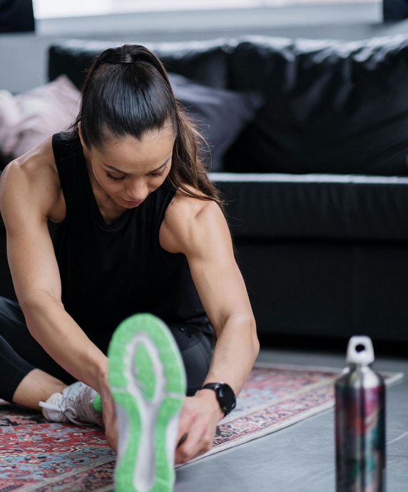 Woman stretching on a yoga mat in a living room, with a water bottle nearby.