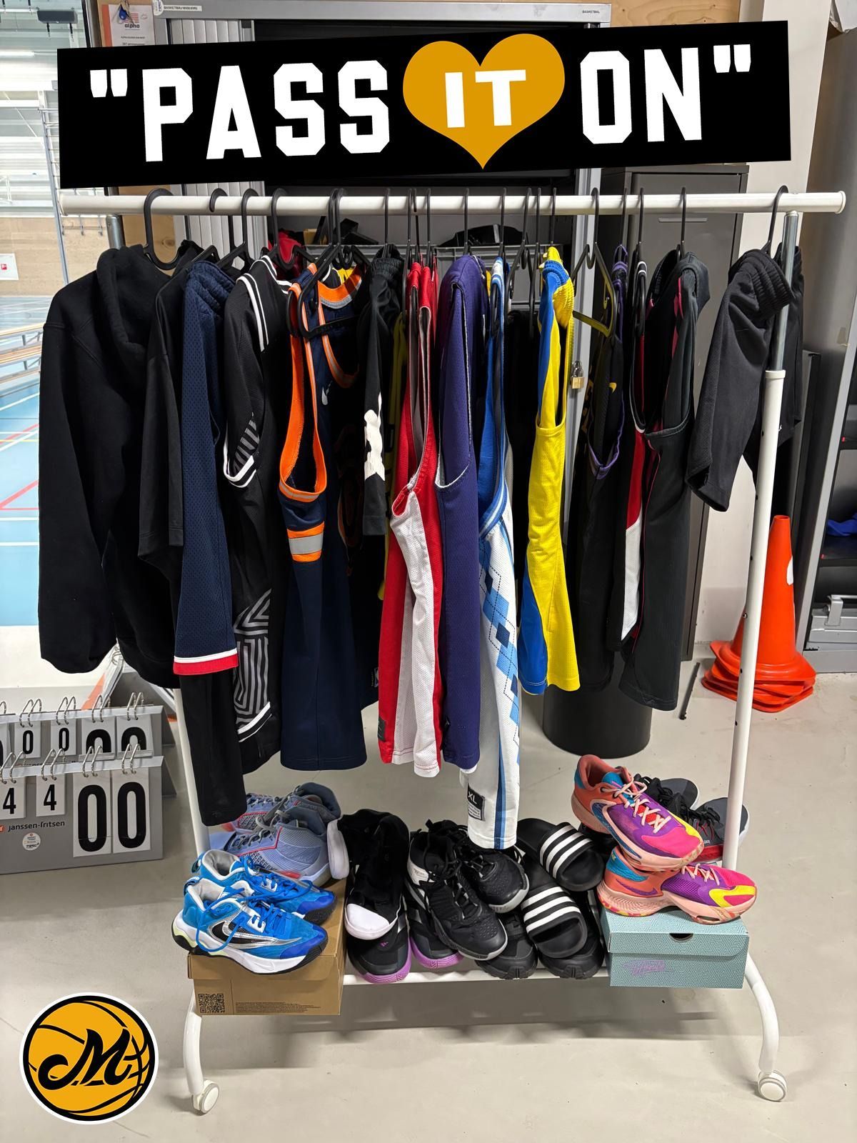 Een kledingrek met diverse jassen en schoenen onder een bordje met 'GEEF HET DOOR' in een winkel.