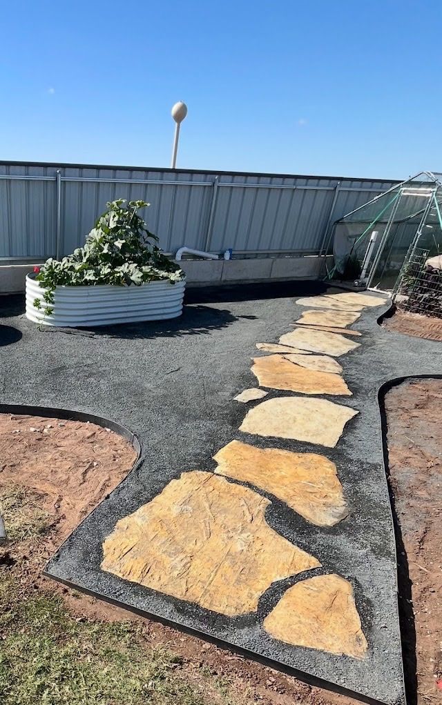 Pathway construction with dark gray pavers, a hammer, and gravel base.