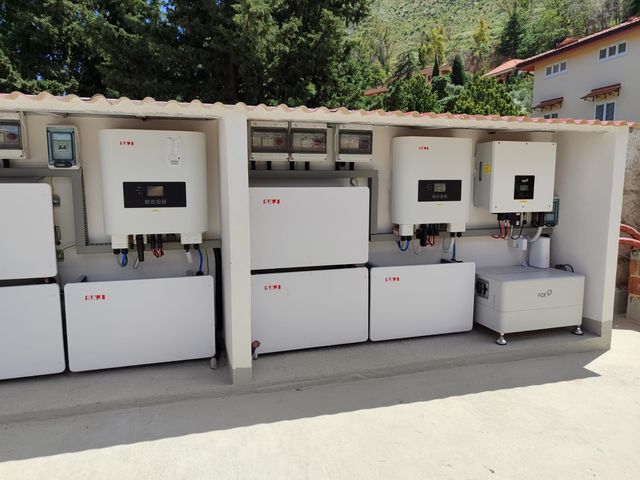All'esterno, una fila di scatole e armadi di controllo elettrici bianchi all'interno di un locale tecnico, con alberi sullo sfondo.