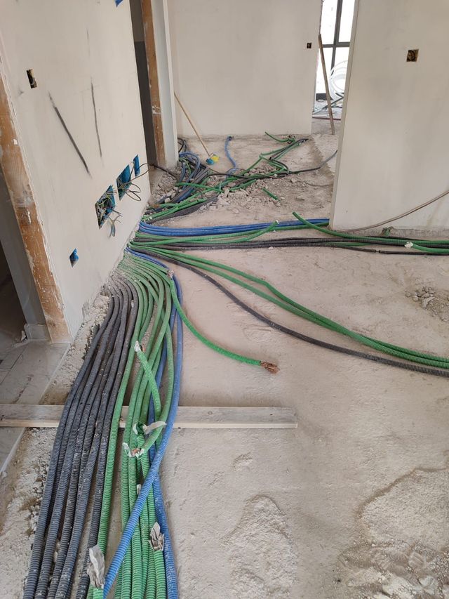 Cavi e tubi sparsi sul pavimento di un corridoio durante i lavori di costruzione di un edificio.