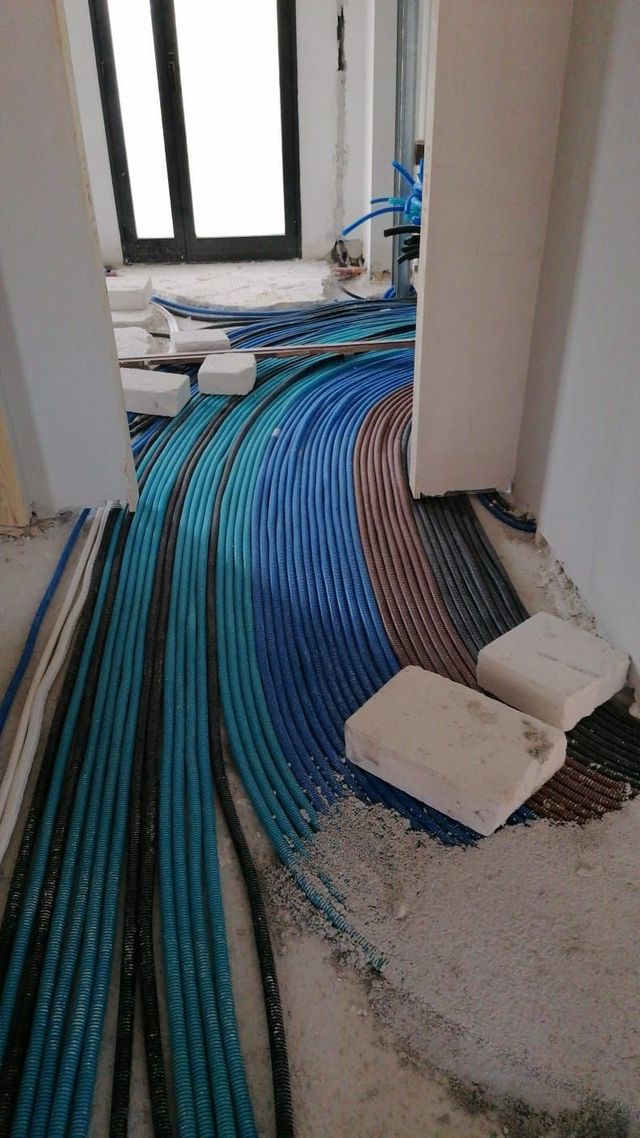 Cavi e tubi sparsi sul pavimento di un corridoio durante i lavori di costruzione di un edificio.