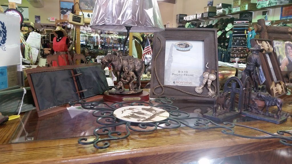 Interior of a store, displaying Western-themed decor like picture frames, figurines, and a lamp on a wooden counter.