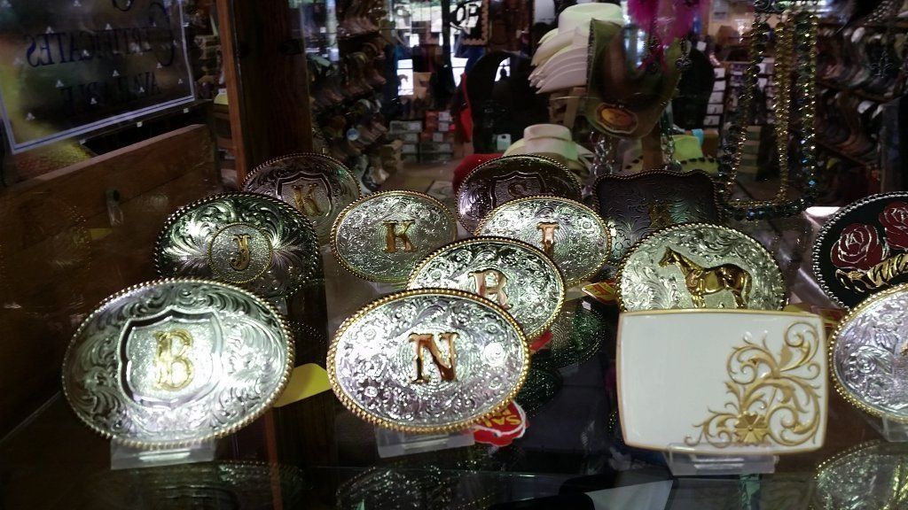 Display of silver and gold belt buckles with western designs in a shop.