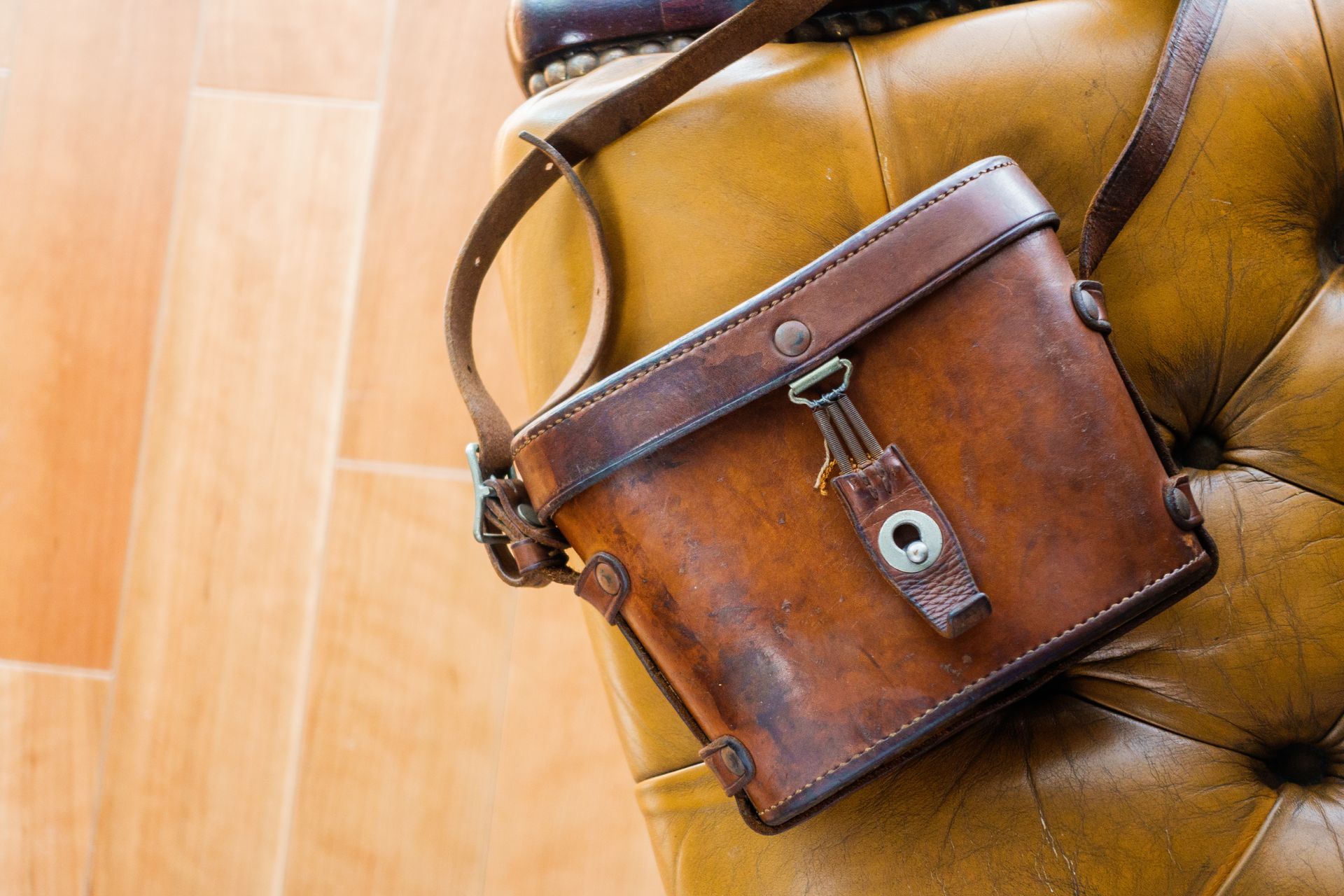 Brown leather camera bag with shoulder strap rests on a tufted, amber-colored surface.