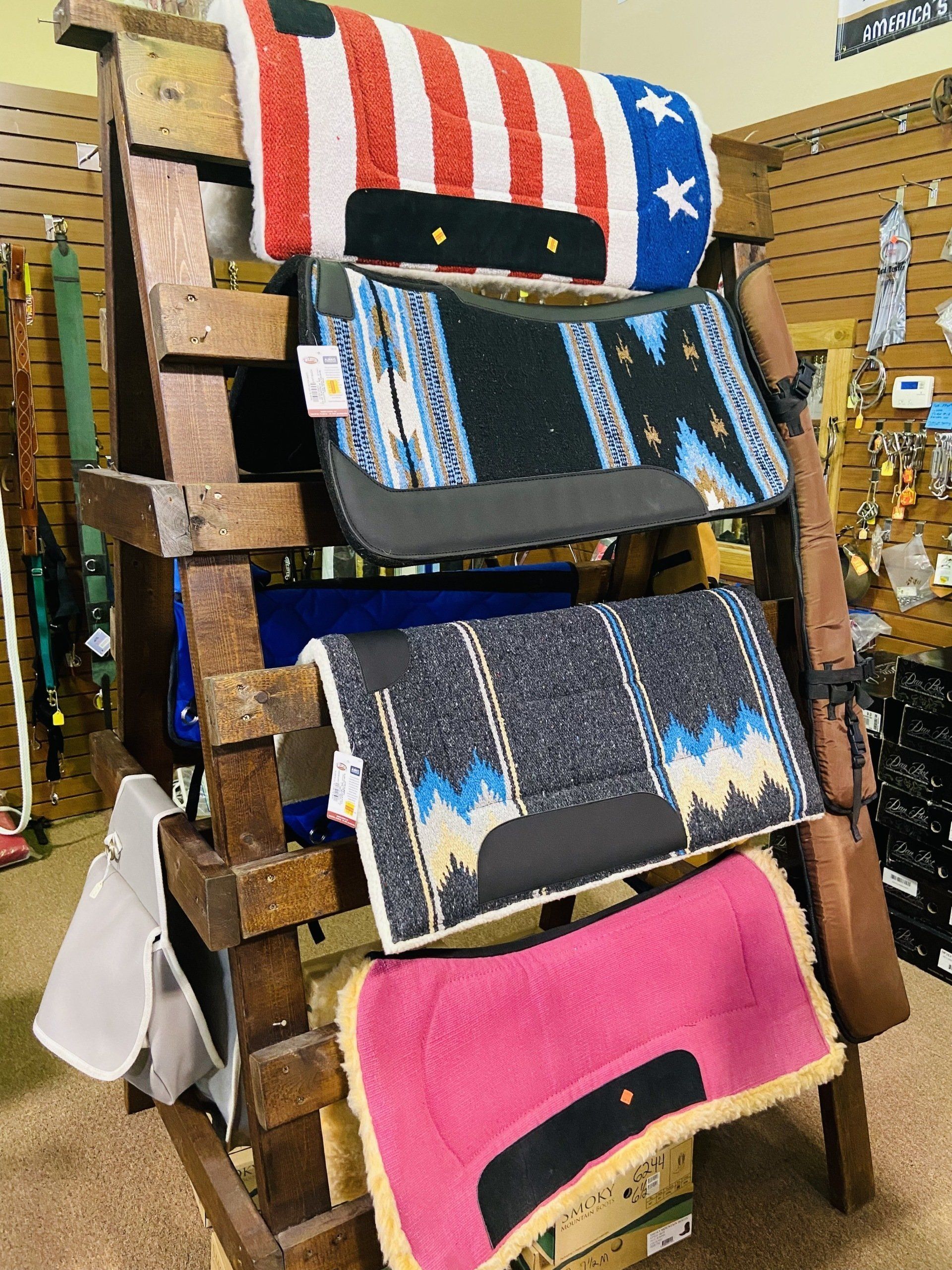 Horse saddle pads on a wooden display rack; various colors and patterns.