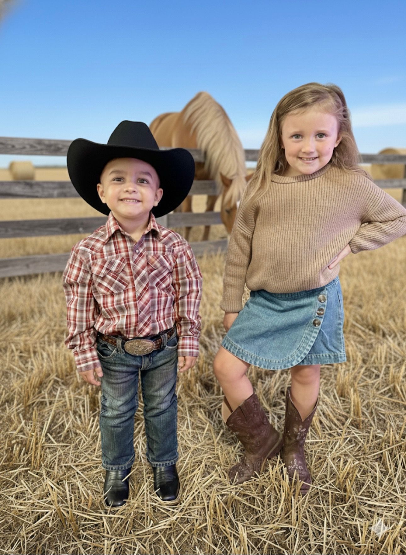 Young boy in cowboy attire, sitting on a trunk with a toy gun. Rustic wood background, holding hand to his face.