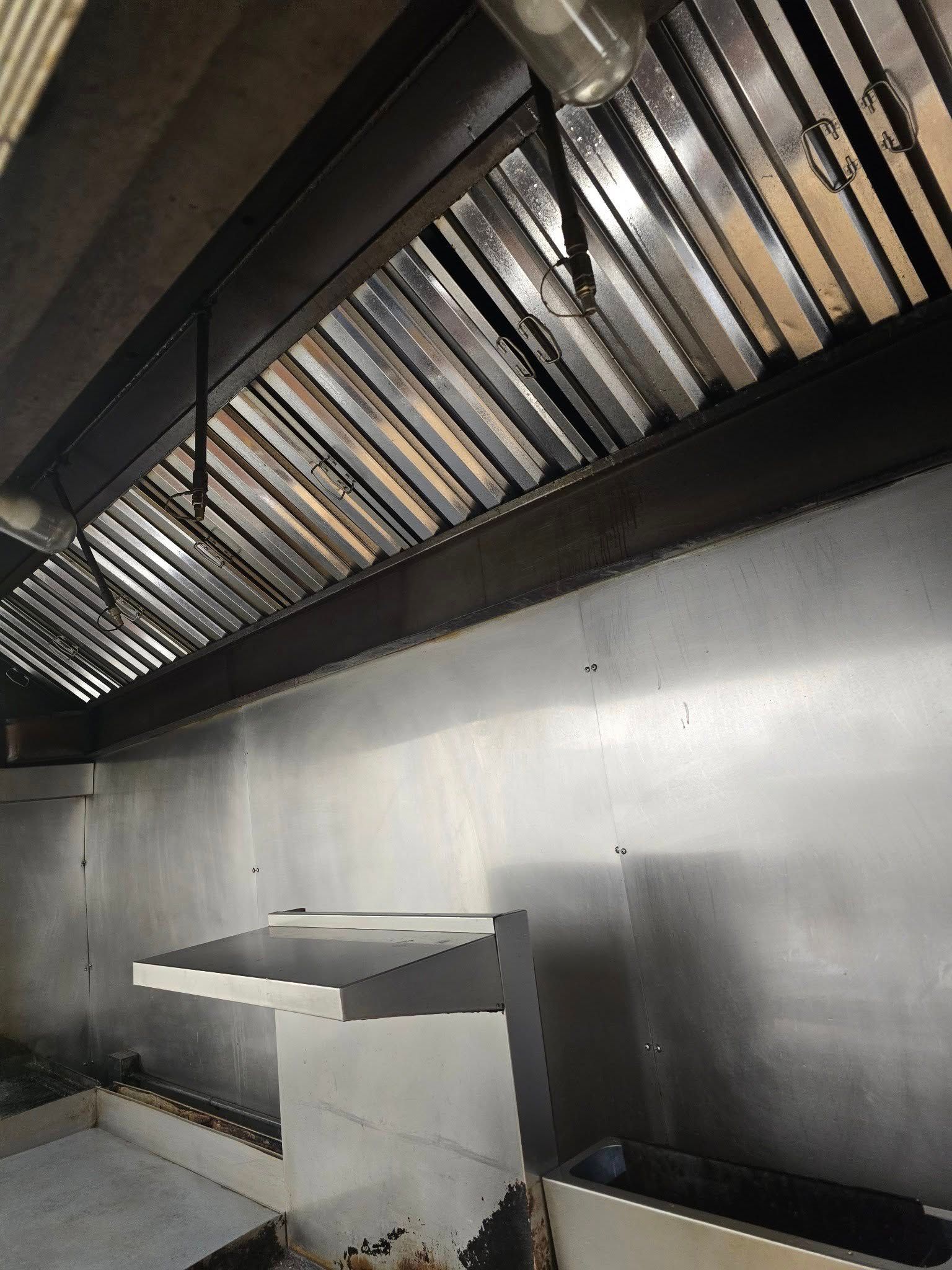 A commercial kitchen exhaust hood with metal grease filters above a stainless steel backsplash and workstation.