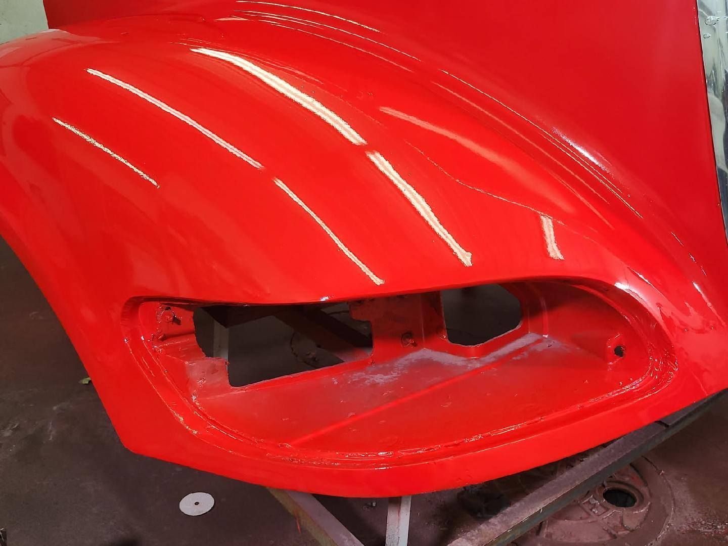 A freshly painted, glossy red car fender with a headlight housing cutout, positioned on a workshop stand.