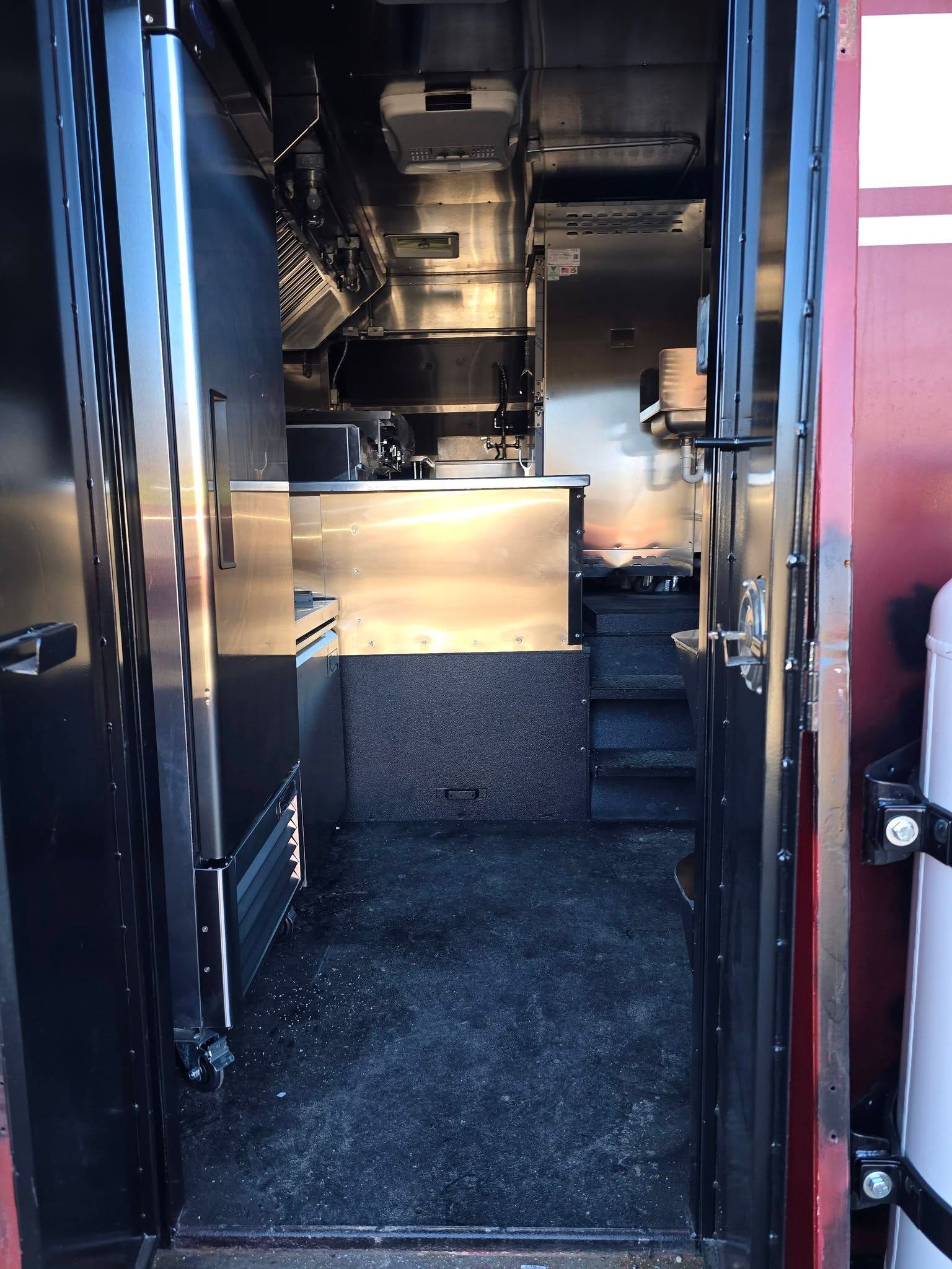 The interior of a food truck kitchen featuring stainless steel equipment, dark gray flooring, and a small set of stairs.