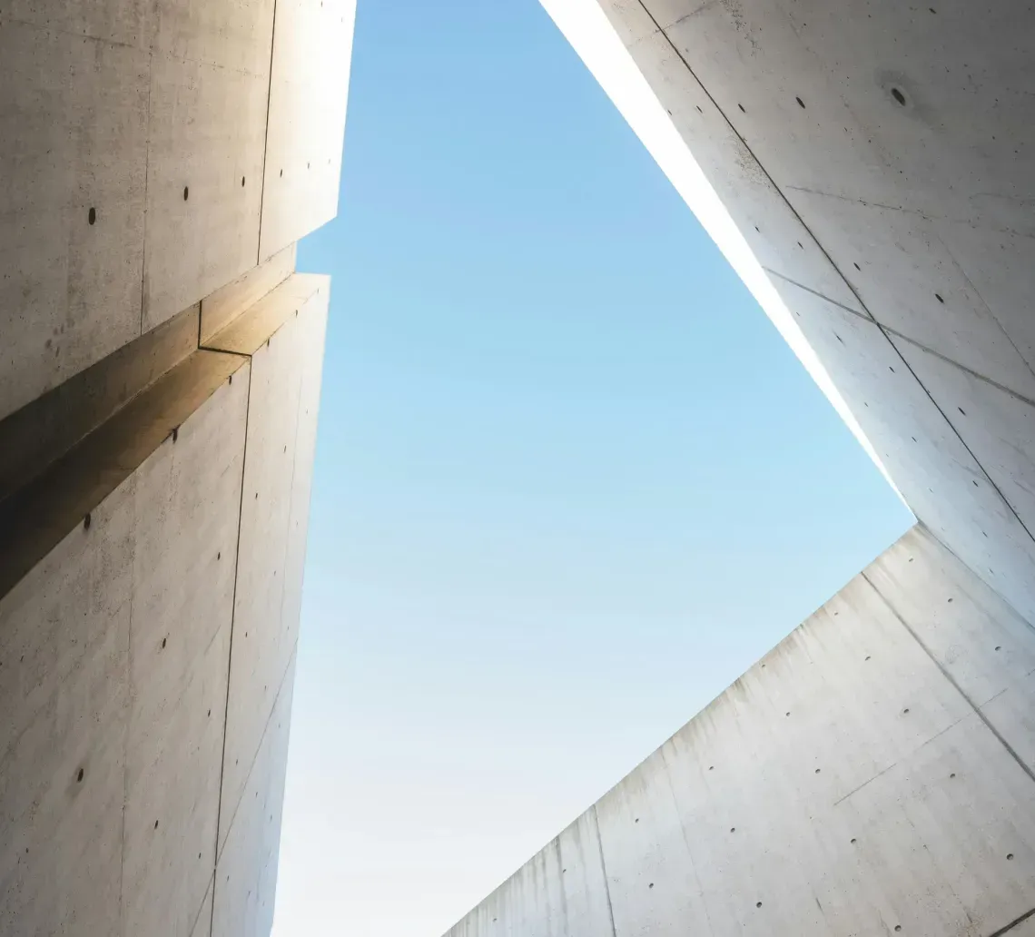 Concrete walls frame a triangular opening to a clear blue sky.