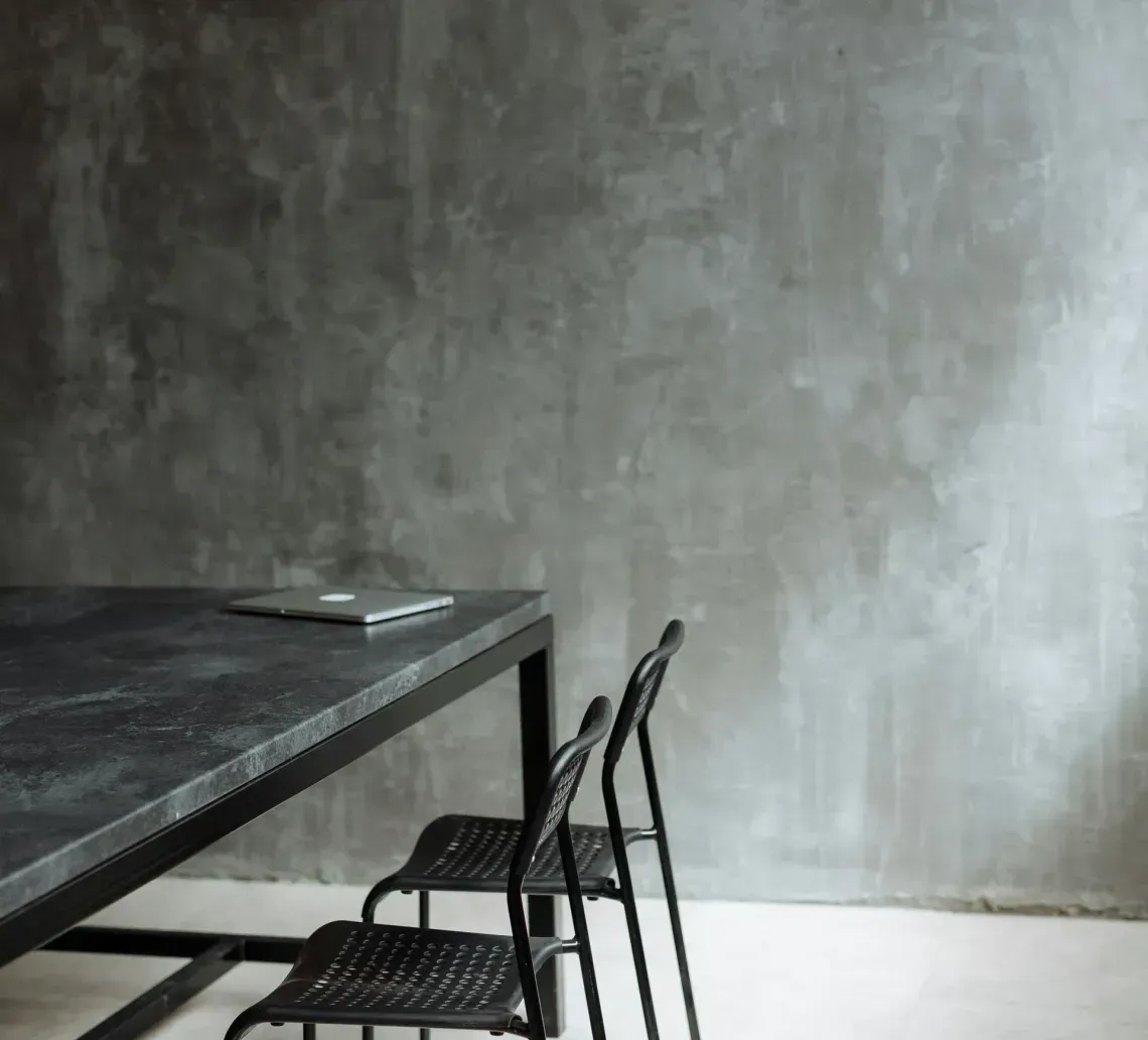 Black table and chairs against a textured gray wall and light floor.
