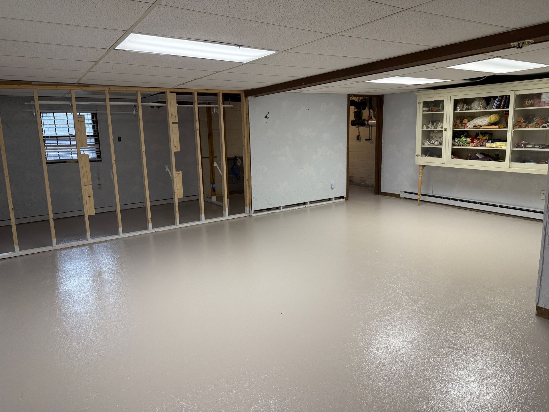 Empty unfinished basement room with exposed studs, white panel wall, and gray speckled floor