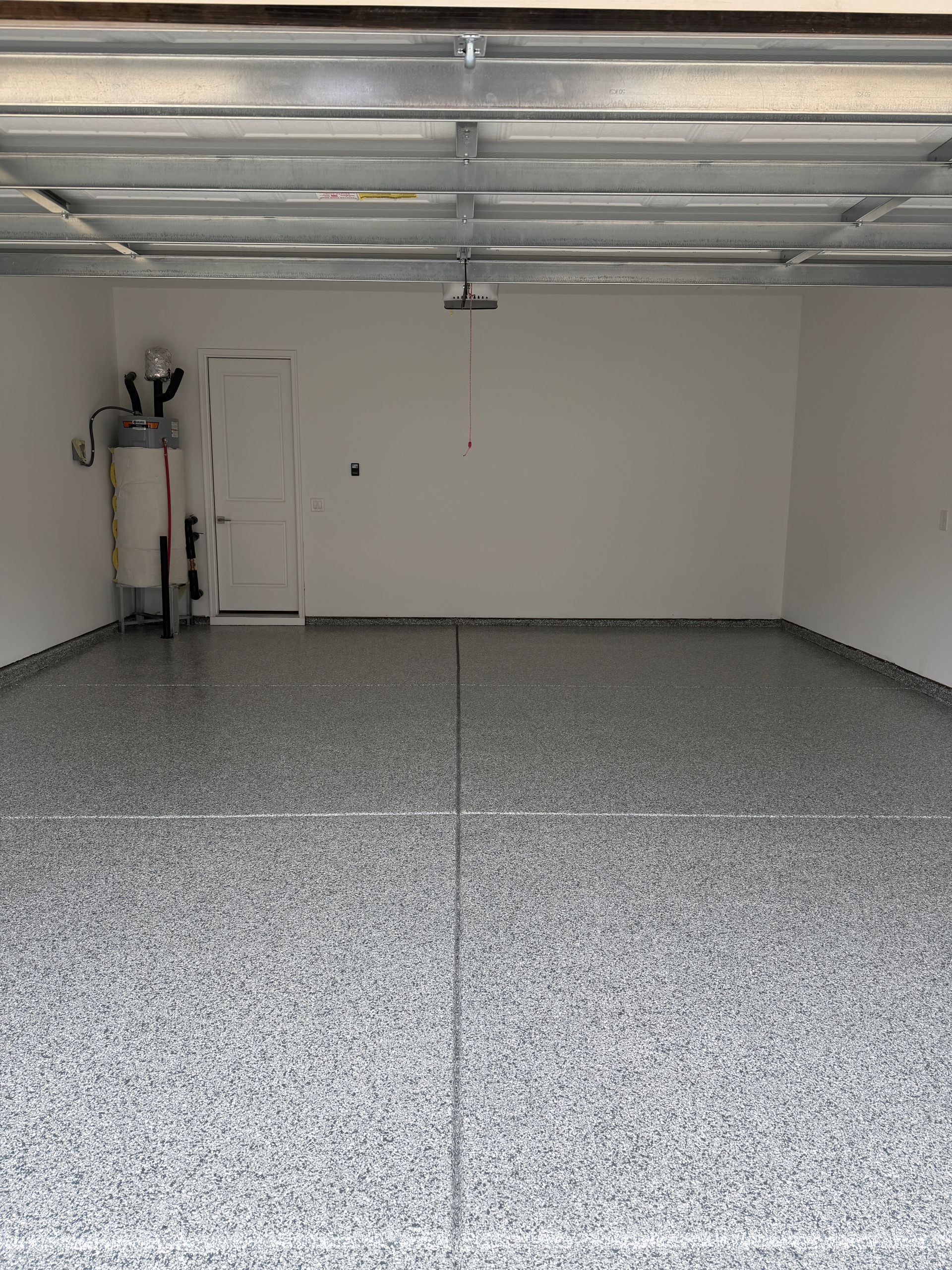 Empty garage with speckled gray floor, white walls, and closed garage door overhead.