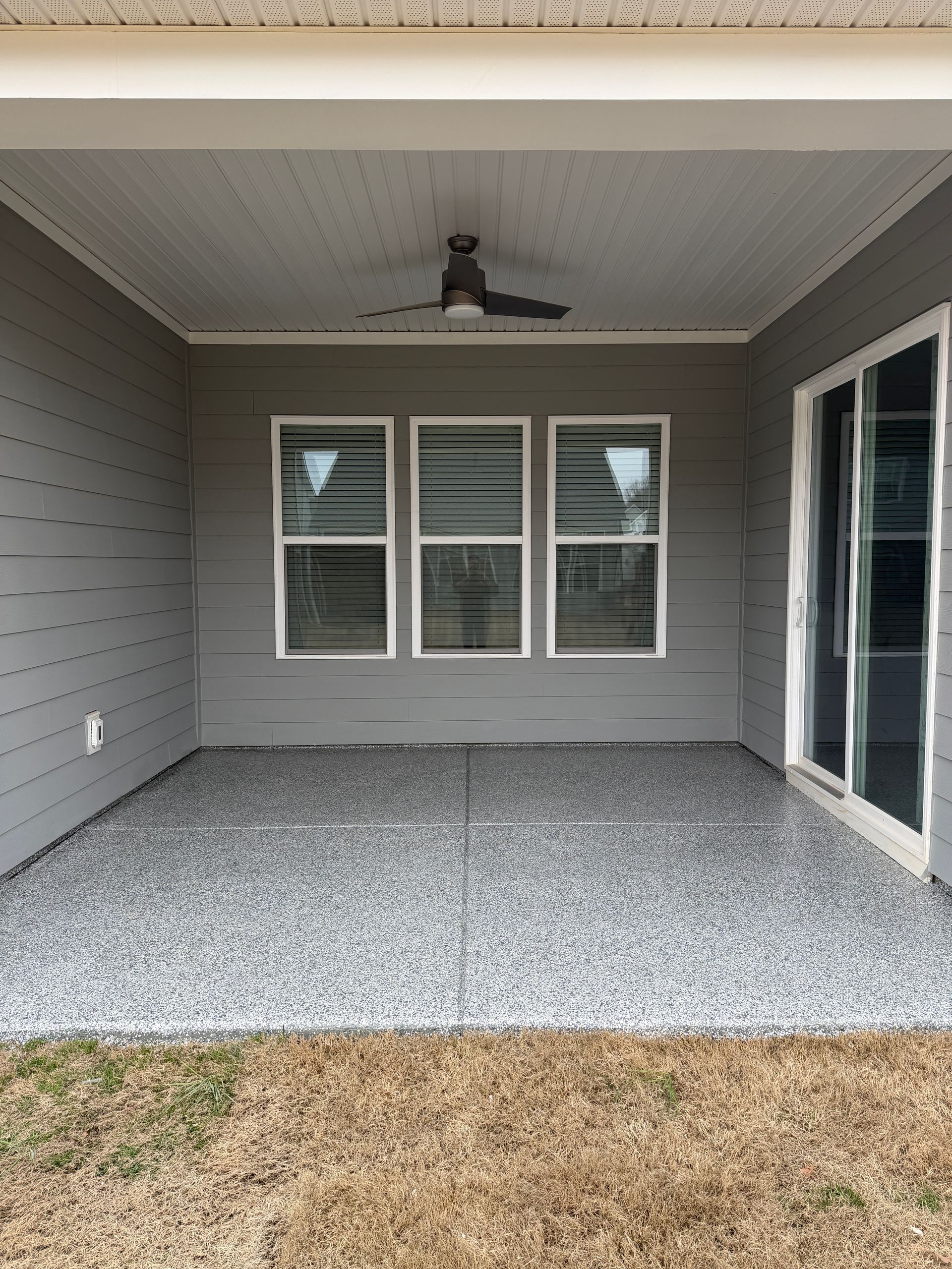Covered patio with gray siding, three windows, a ceiling fan, and a speckled floor.