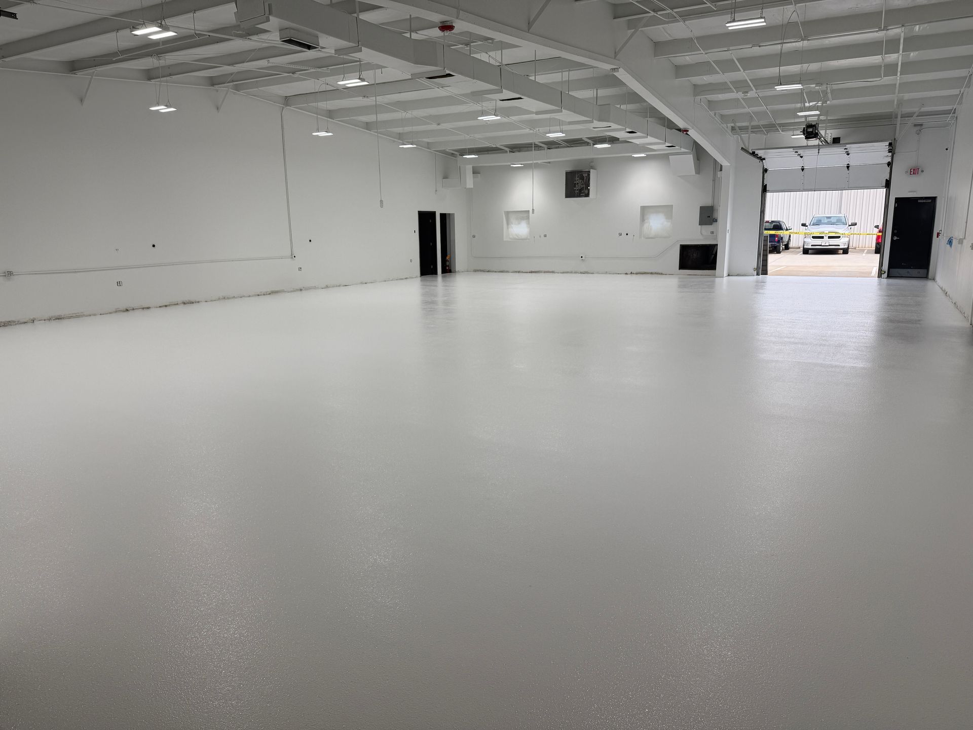 Large empty white warehouse interior with a wide open garage door letting in daylight