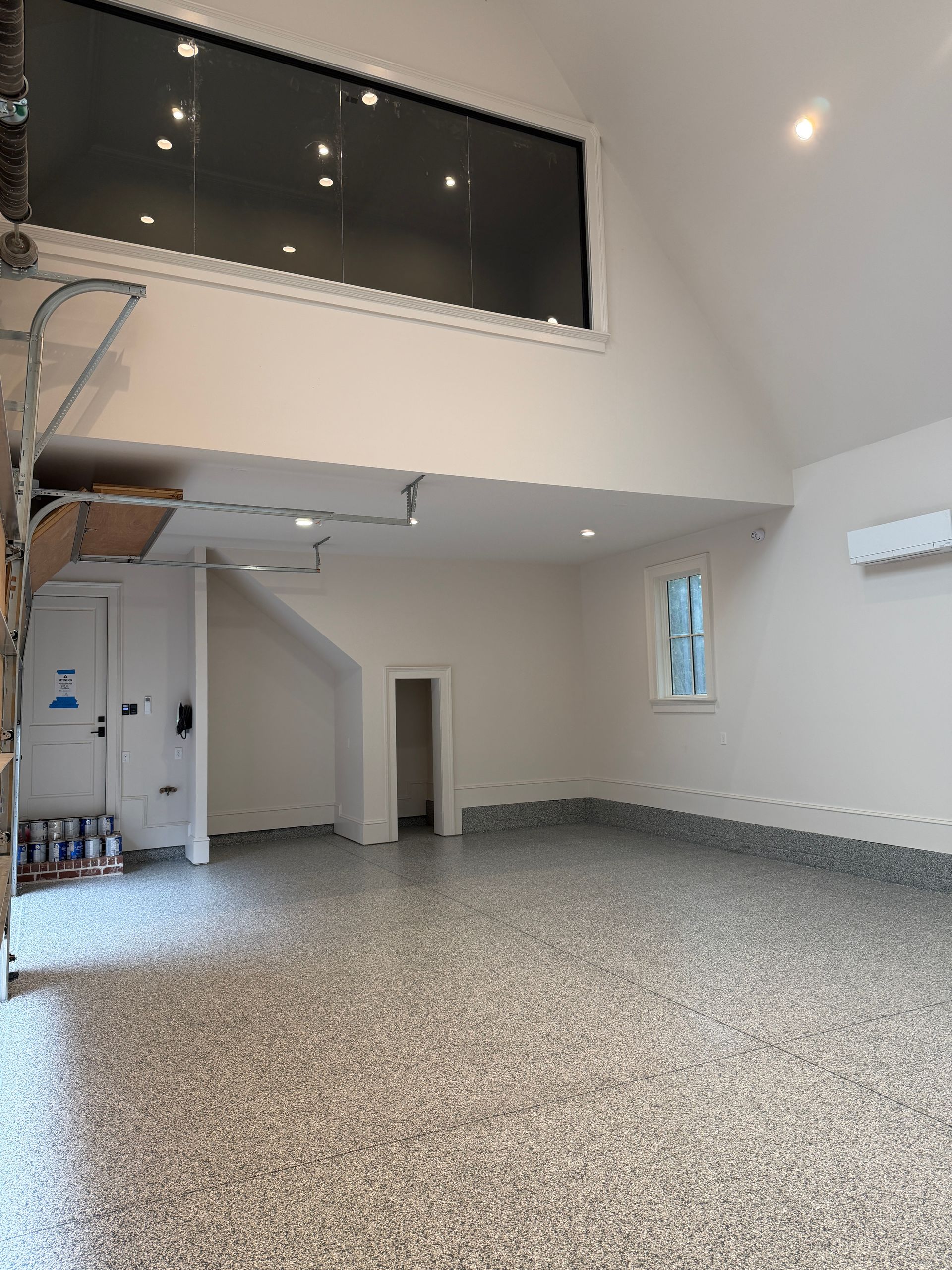 Empty modern living room with high ceilings, mezzanine railing, and speckled floor.