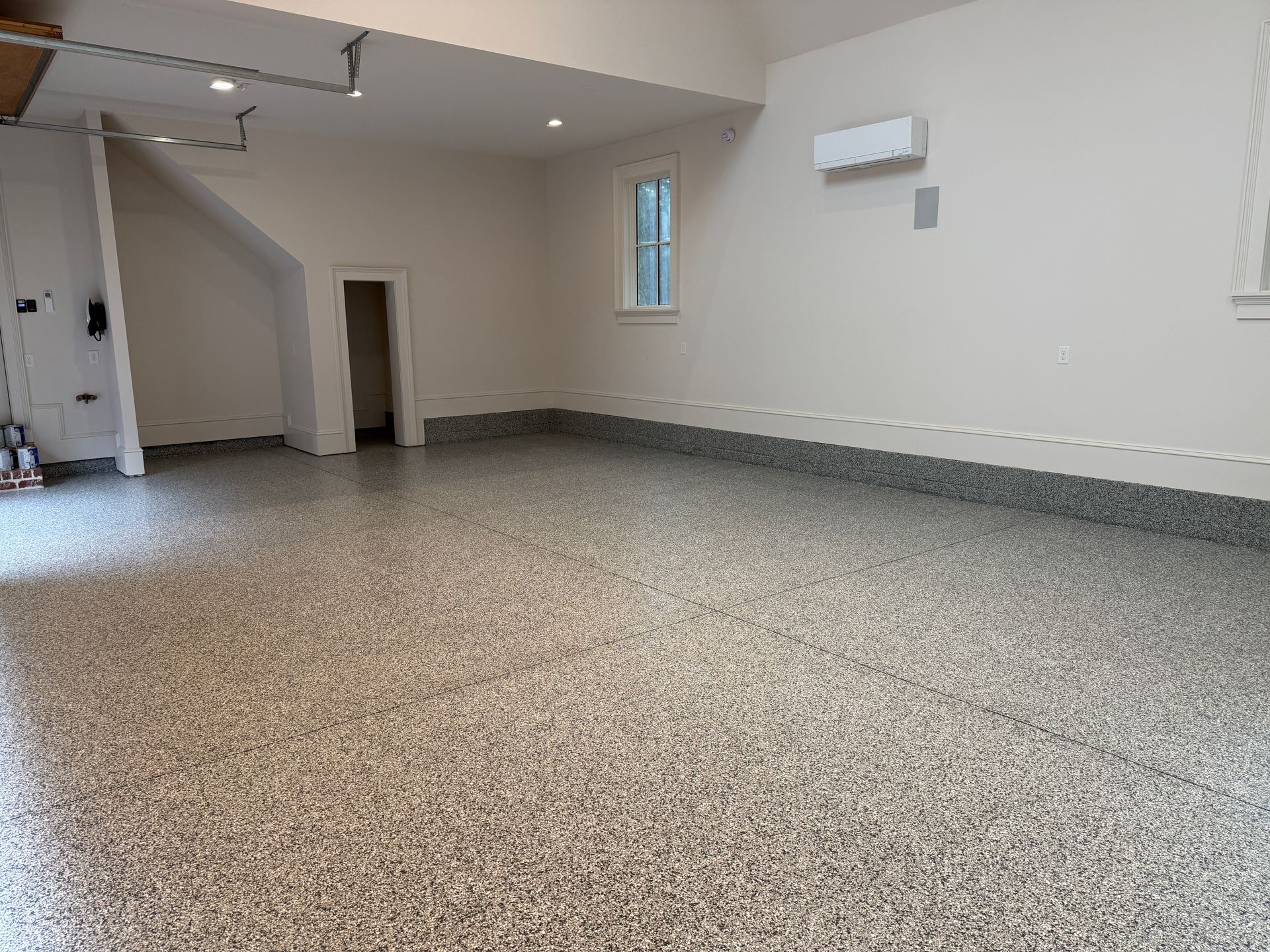 Empty garage with speckled epoxy floor, white walls, and a small window.