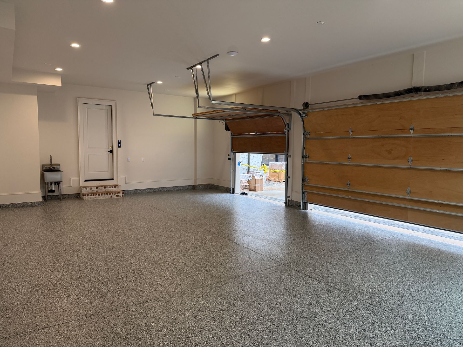 Empty garage with speckled floor, white walls, and an open overhead door letting in daylight.