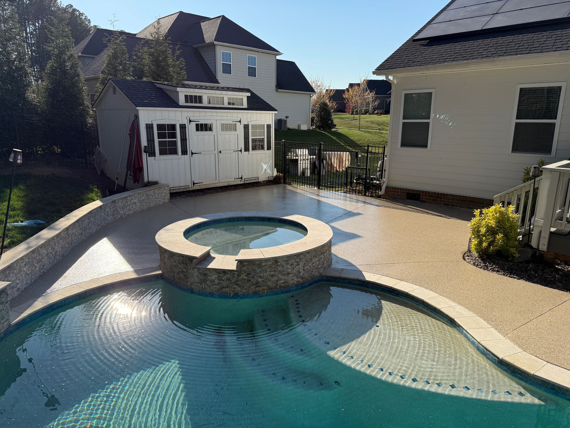 Backyard pool with stone hot tub, white shed, and house in the background