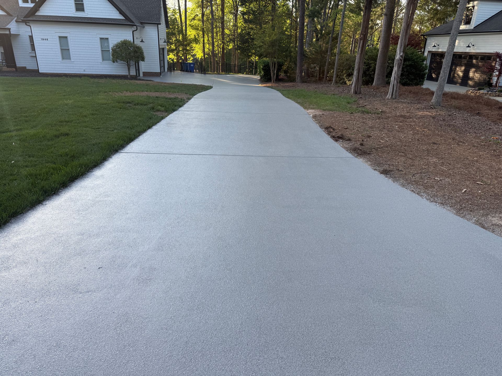 Freshly poured concrete driveway beside a white house and wooded yard at dusk