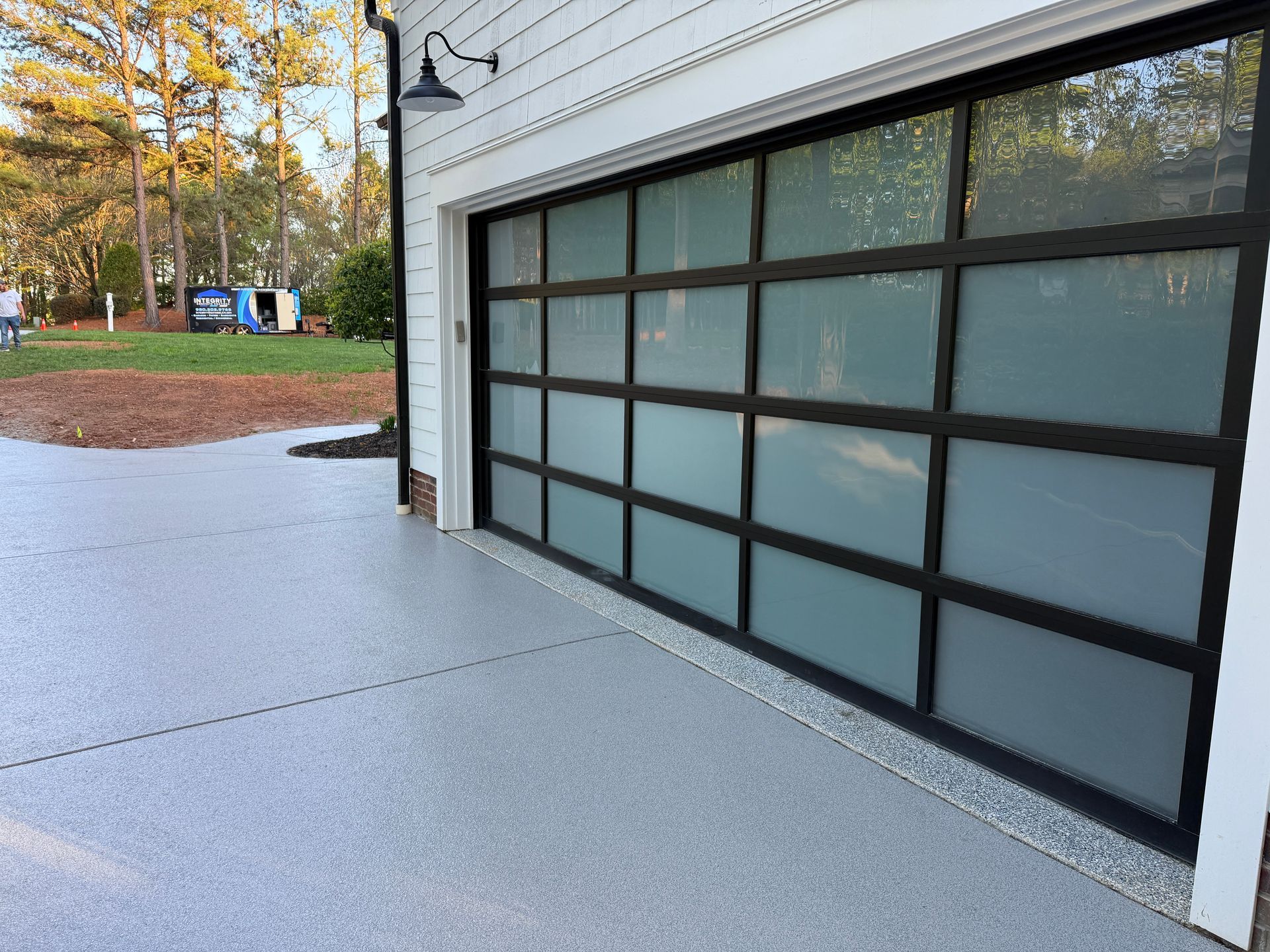 Modern garage door with frosted glass panels beside a light concrete driveway and autumn trees