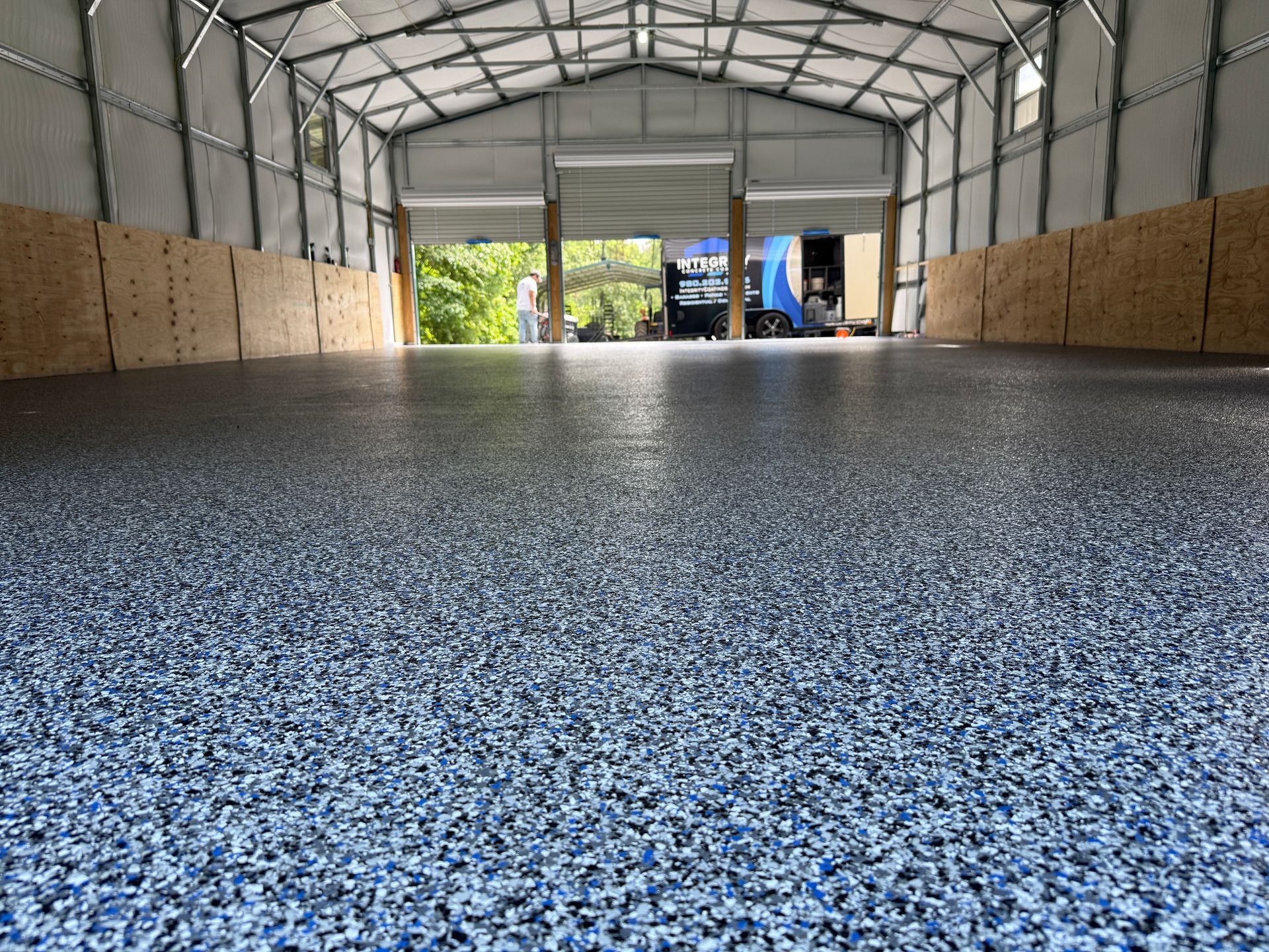 Empty indoor warehouse with speckled epoxy floor, metal roof, and open doorway showing daylight outside