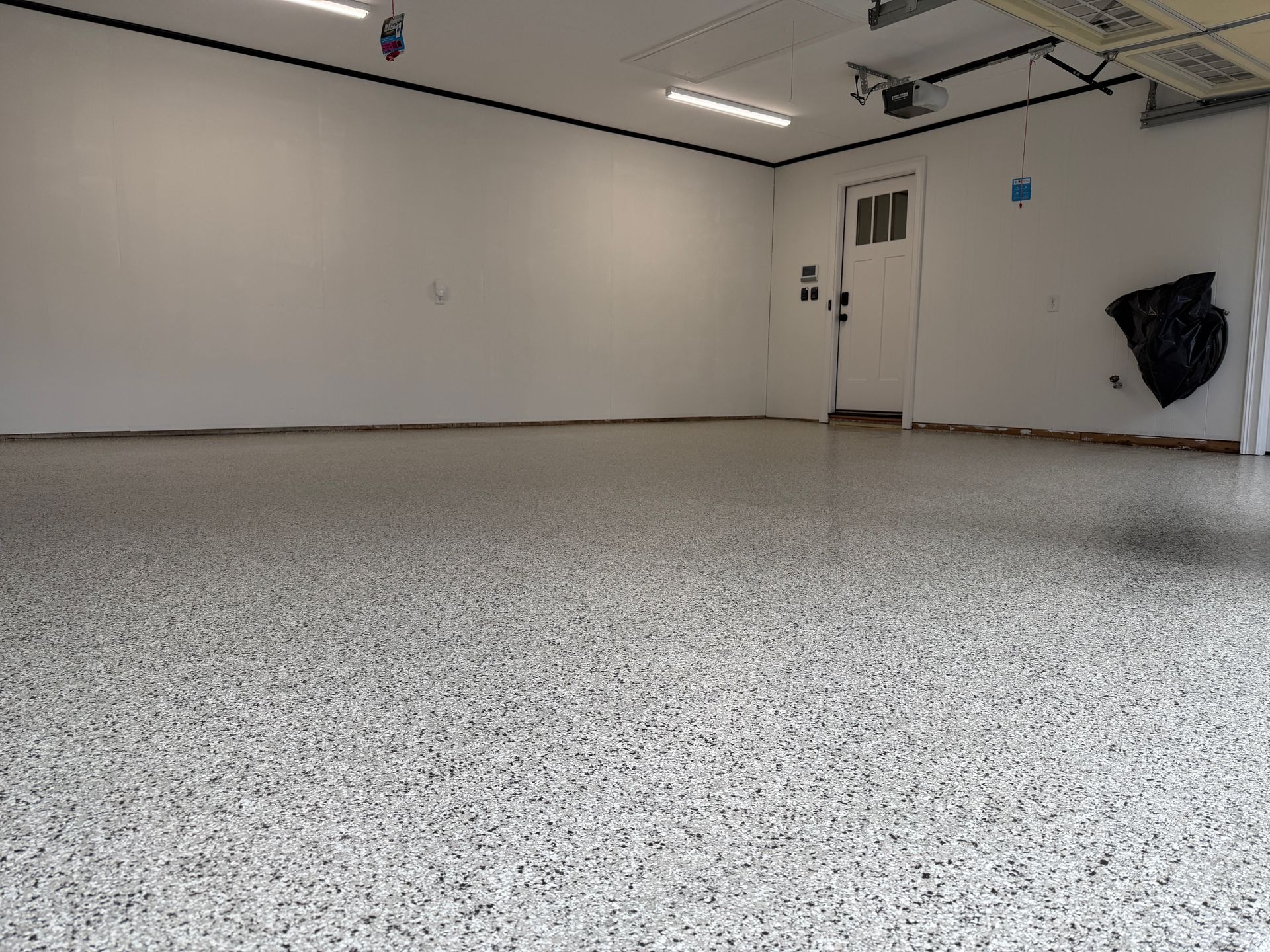 Empty garage with white walls, speckled gray floor, and a side door on the right.