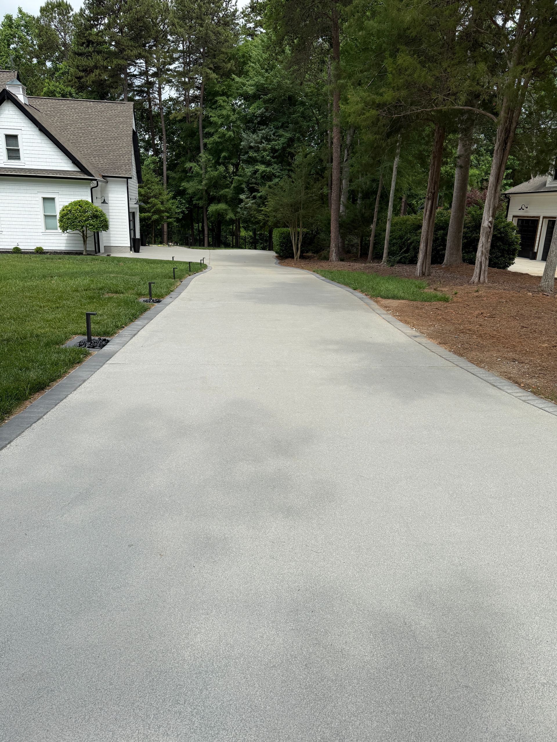 Gravel driveway beside a white house, leading into a wooded area with trees and mulch.