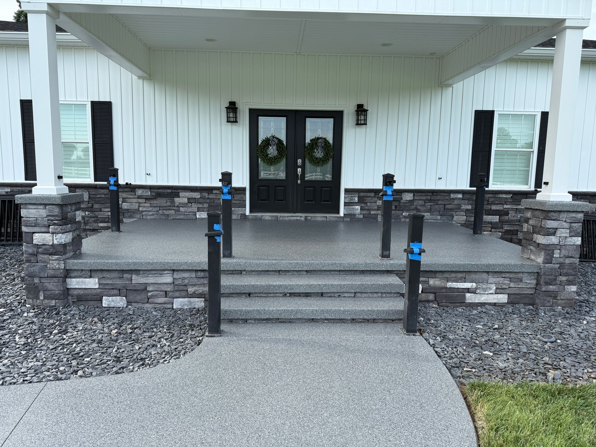Front entrance with double doors, steps, railings, and blue-lit posts beneath a covered porch