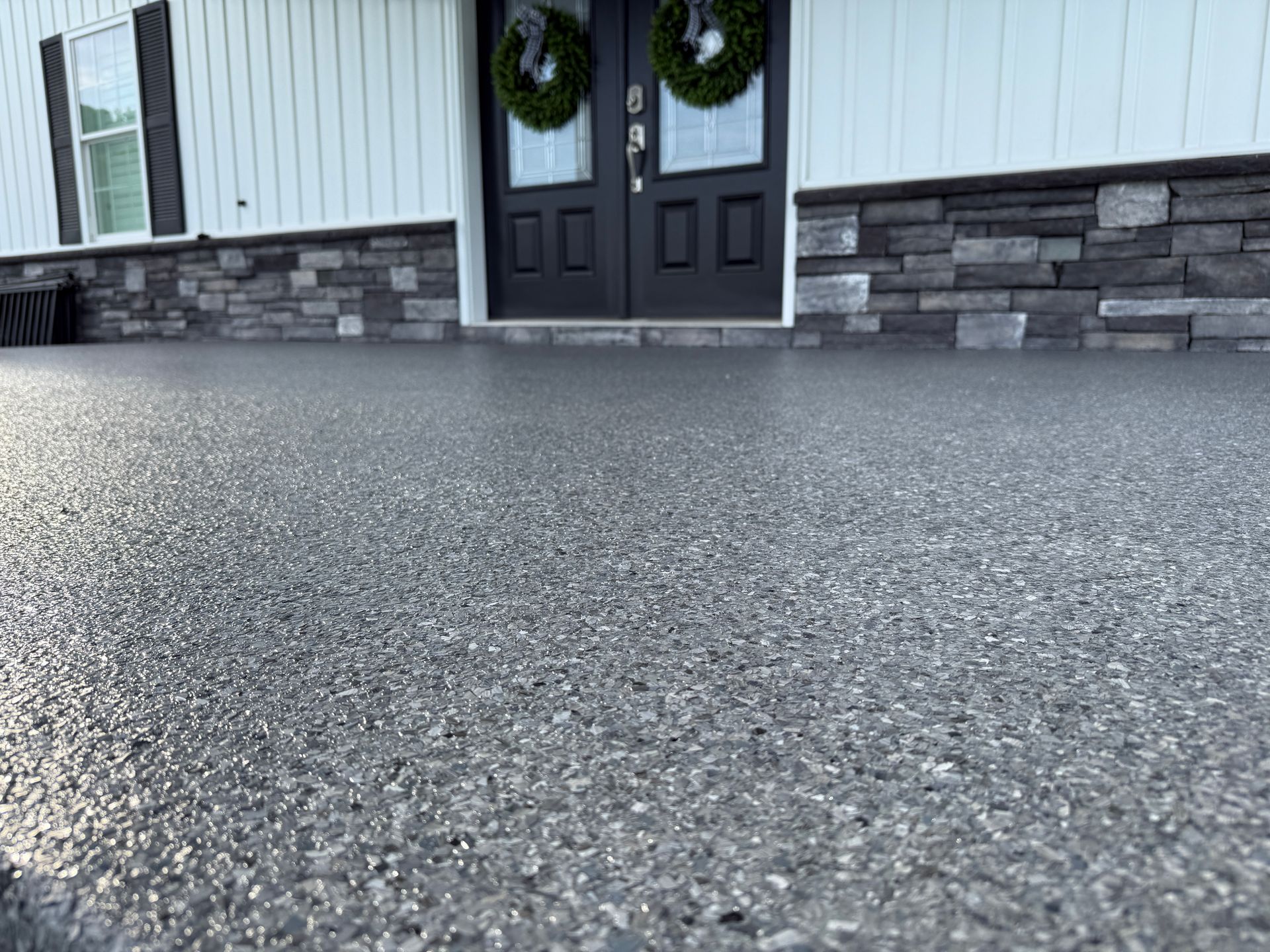 Front porch with double black doors, stone base, white siding, and a wreath.