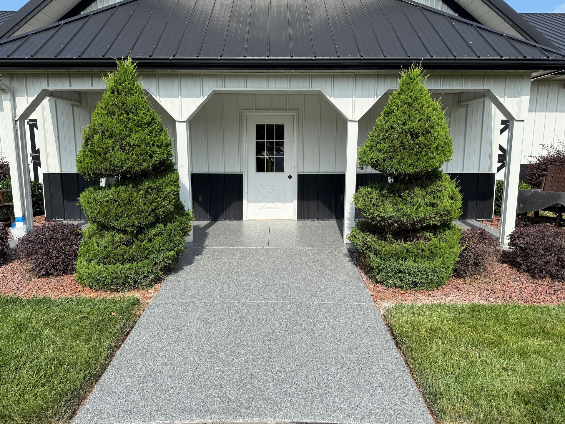 Front entrance of a white building with a gray walkway and manicured shrubs.