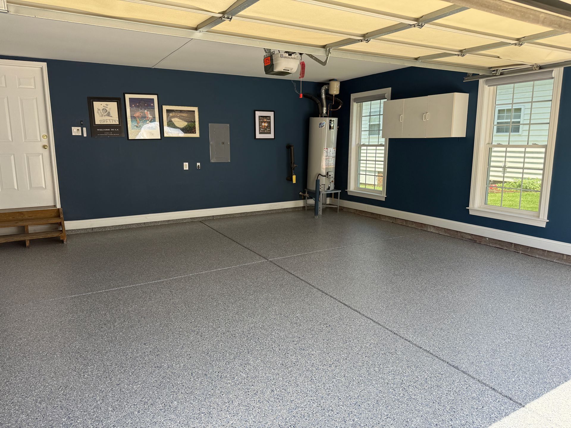 Empty carpeted room with dark blue walls, framed pictures, and large windows letting in daylight