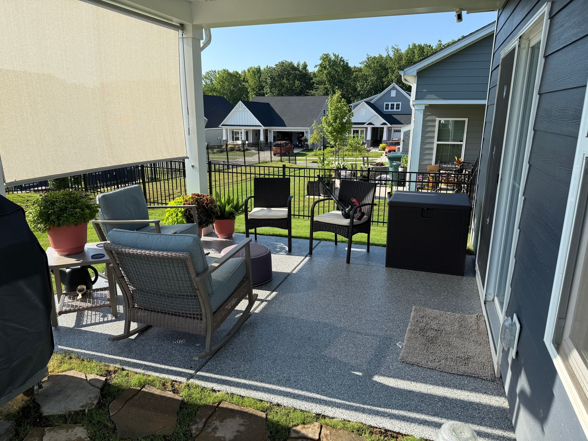 Covered patio with outdoor chairs, small tables, and potted plants overlooking a backyard and neighboring houses.