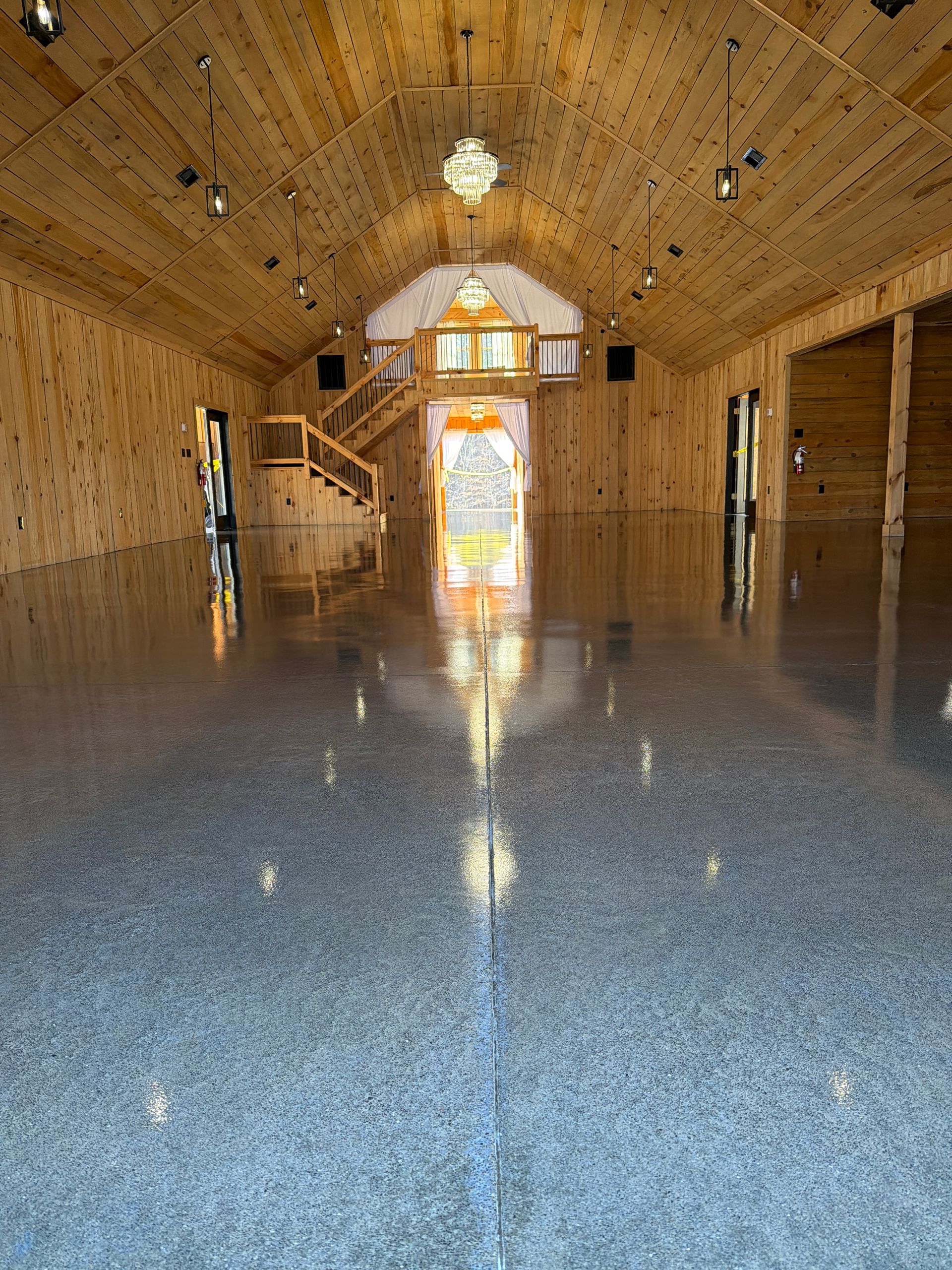 Empty wooden chapel interior with glossy floor, vaulted ceiling, and bright doorway at the far end