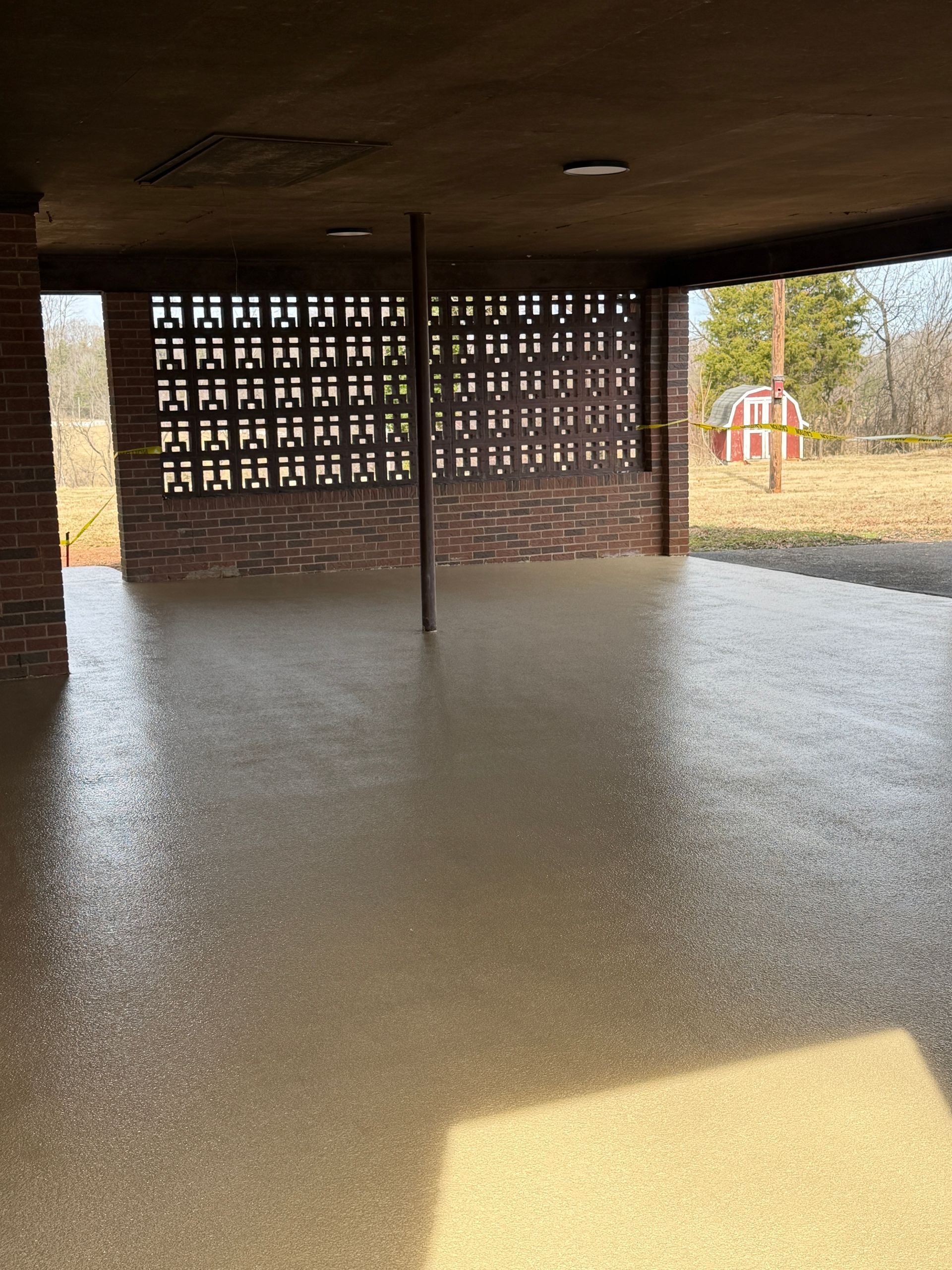 Covered outdoor patio with a wet concrete floor and brick walls, lit by sunlight from the right.