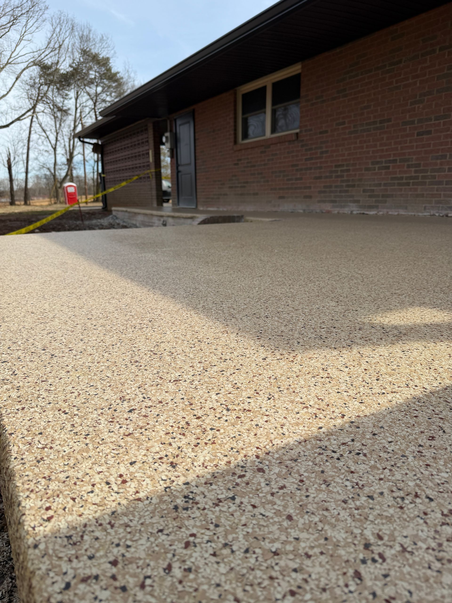 Low-angle view of a brick building with a gravel foreground and trees in the background