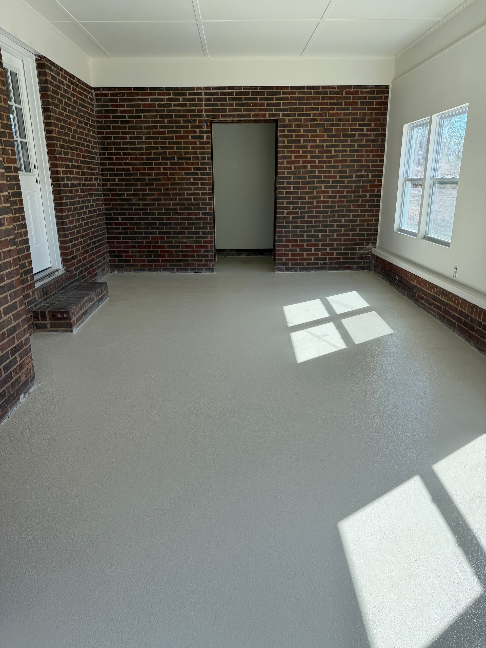 Empty sunlit brick room with gray carpet and windows, light streaming onto the floor