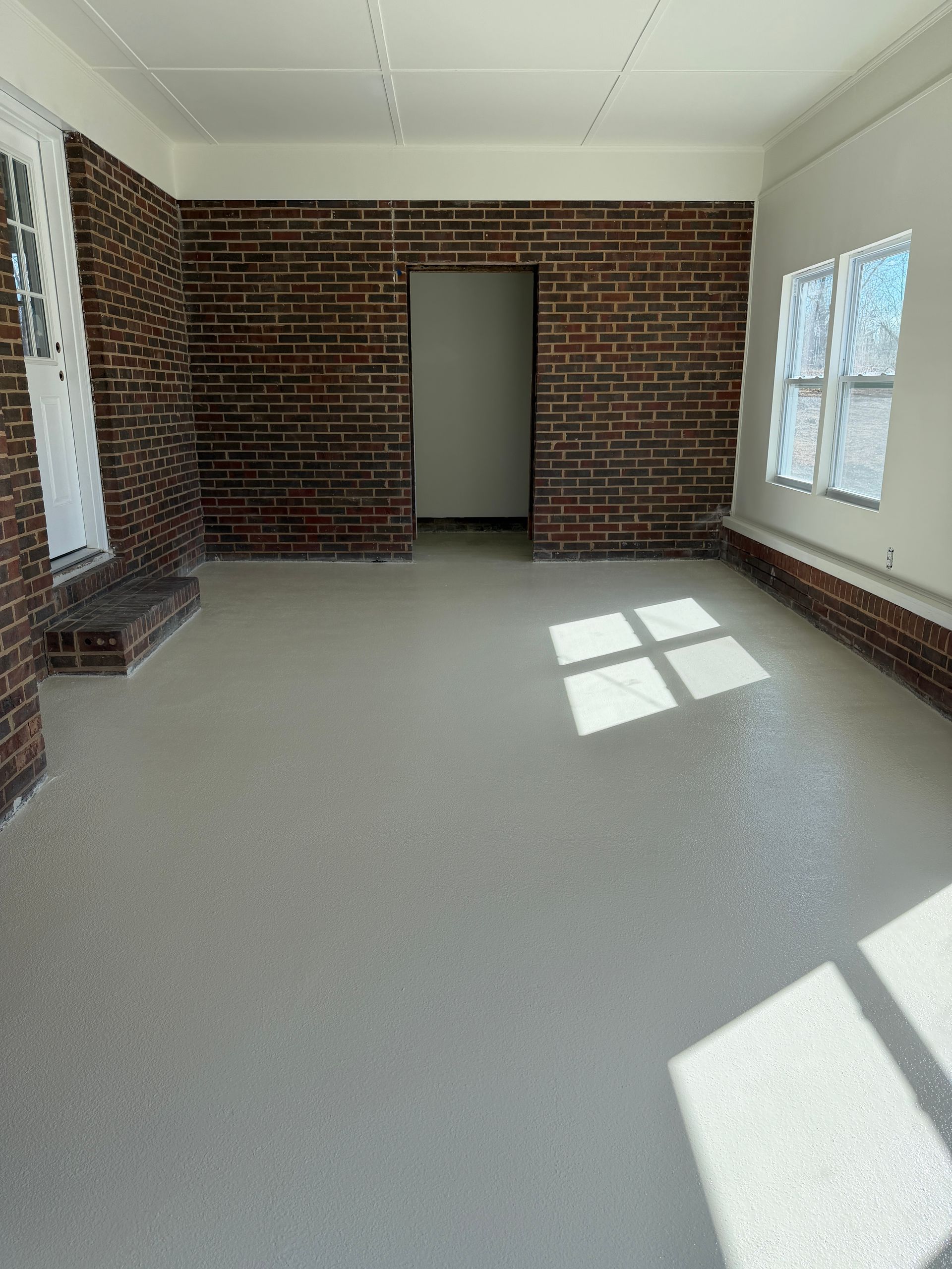 Empty room with brick accent wall, large windows, and sunlight on the floor