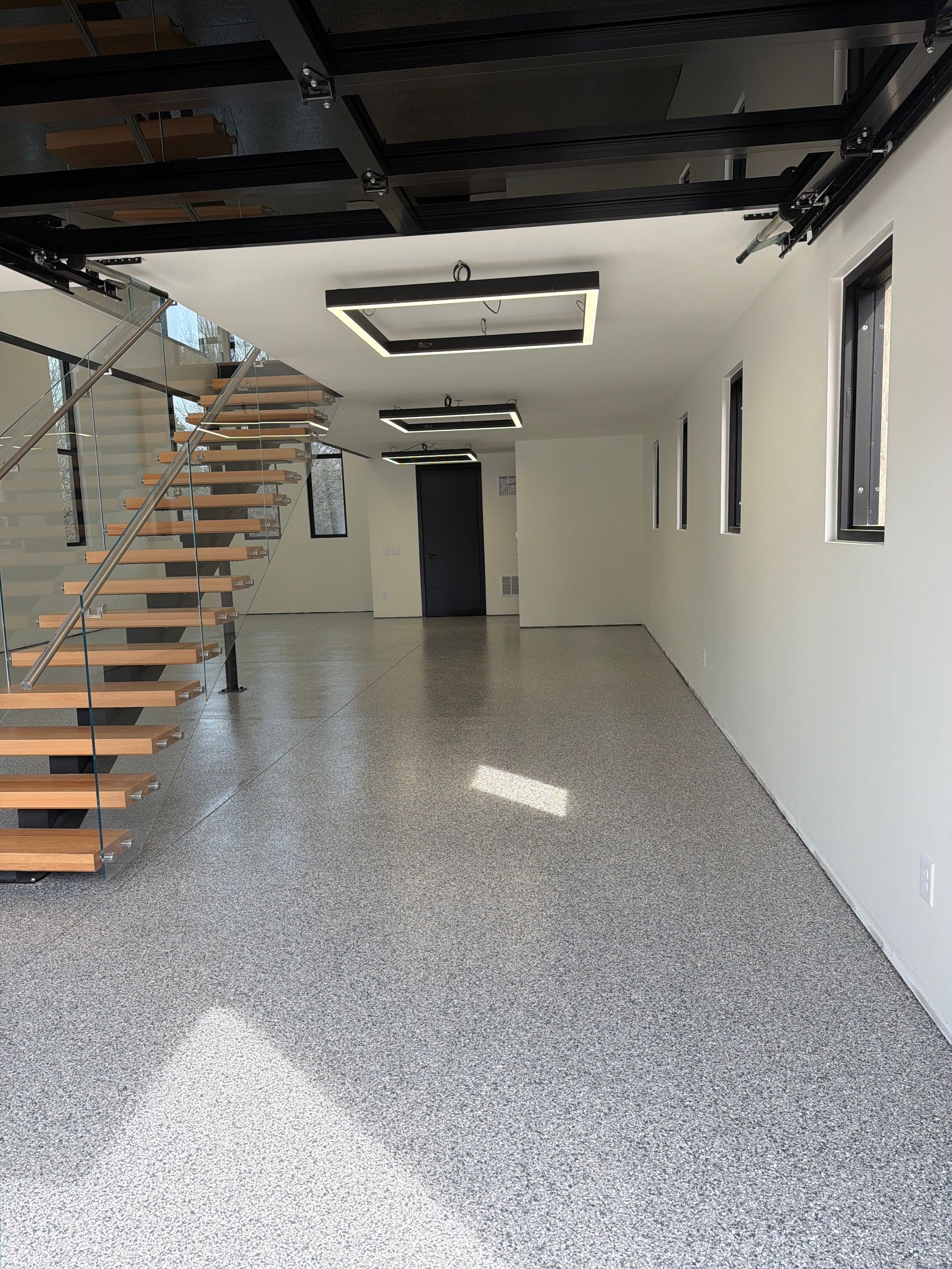 Empty modern interior with staircase, white walls, speckled floor, and skylight from above