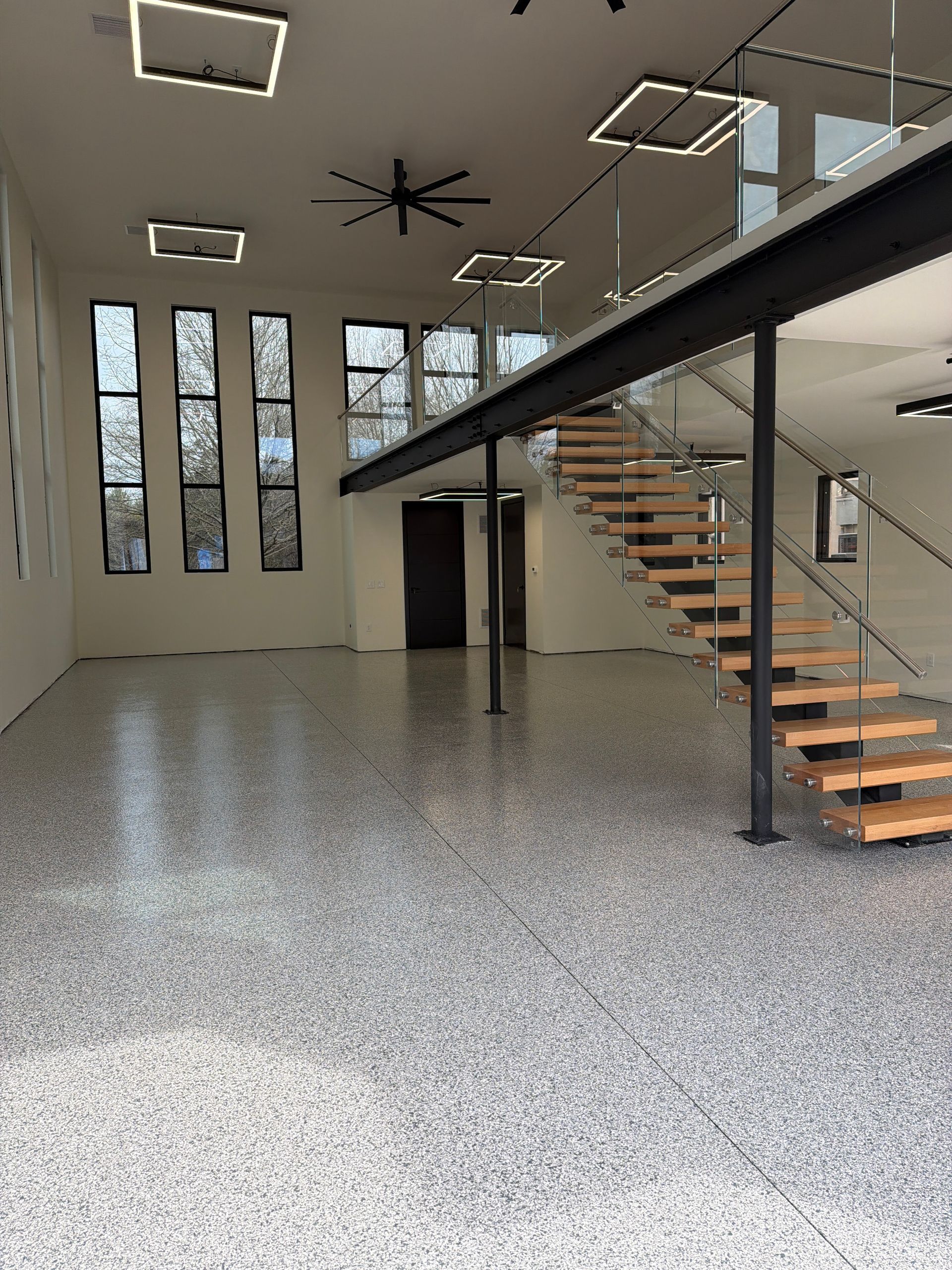 Modern interior with polished concrete floor, tall windows, and a black metal staircase mezzanine.