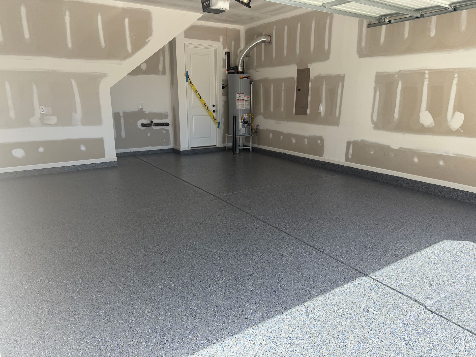 Empty garage with gray epoxy floor, unfinished drywall, and bright sunlight coming through the open door