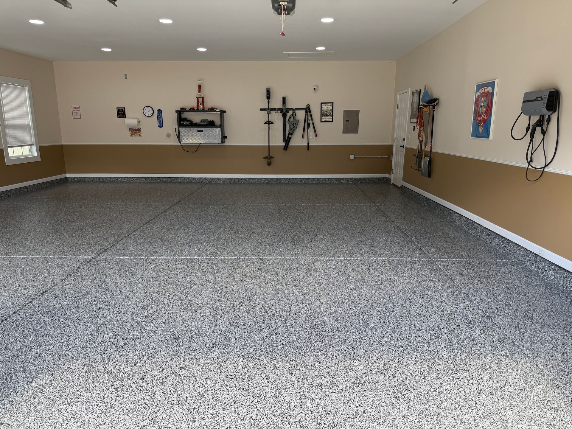 Empty garage-style room with speckled floor, beige walls, and wall-mounted tools and equipment