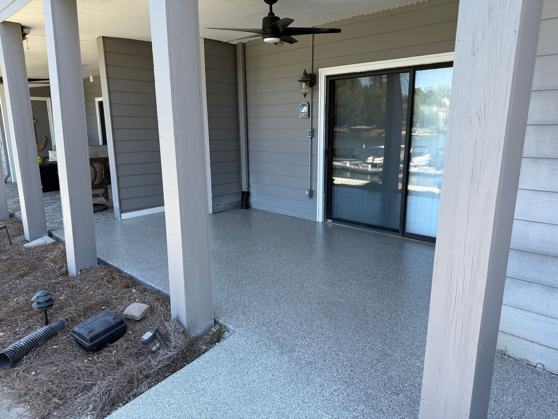 Covered apartment patio with ceiling fan, sliding glass door, and white support columns.