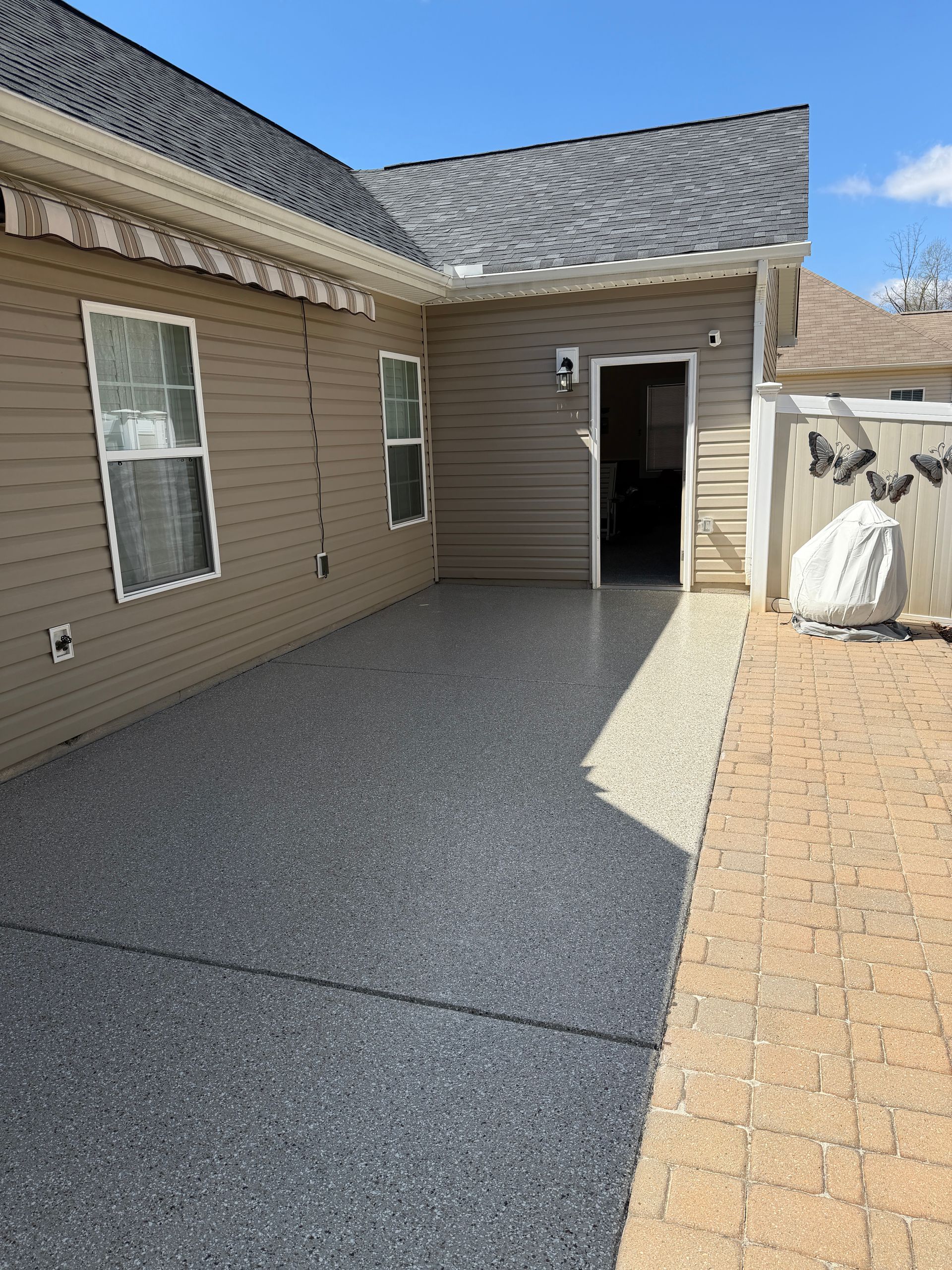 Side yard with beige house siding, gravel patio, and open back door beside a brick walkway