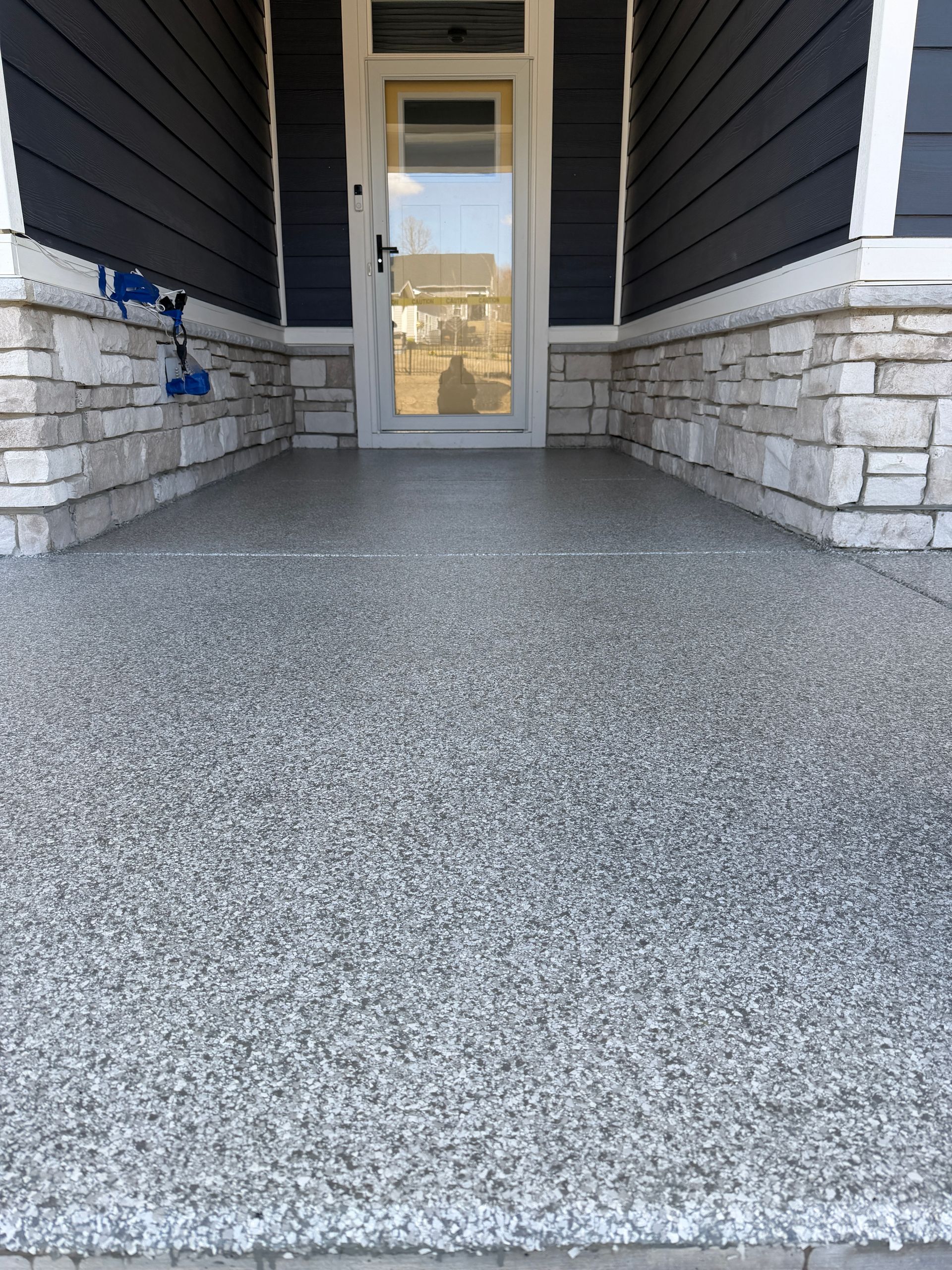 Front porch with speckled gray flooring, stone half-walls, dark siding, and a glass front door.