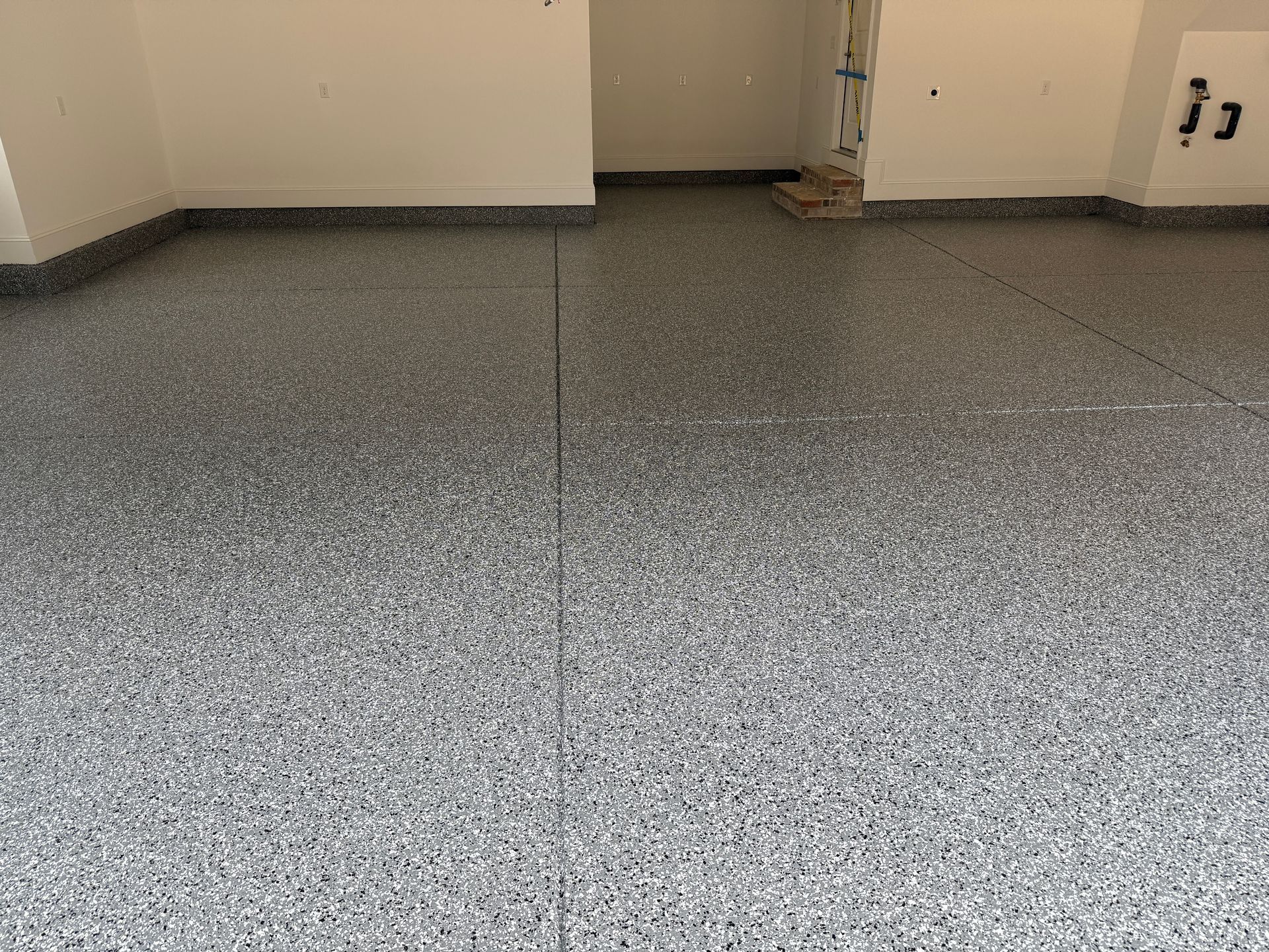 Empty speckled gray floor in a bare room with beige walls and a doorway opening.