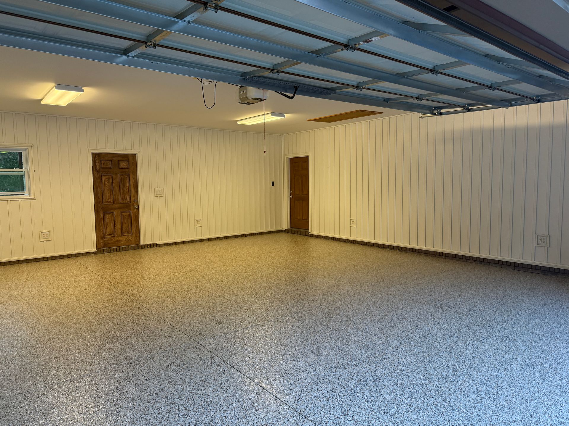 Empty indoor room with white paneled walls, gray speckled floor, blue ceiling, and two wooden doors.