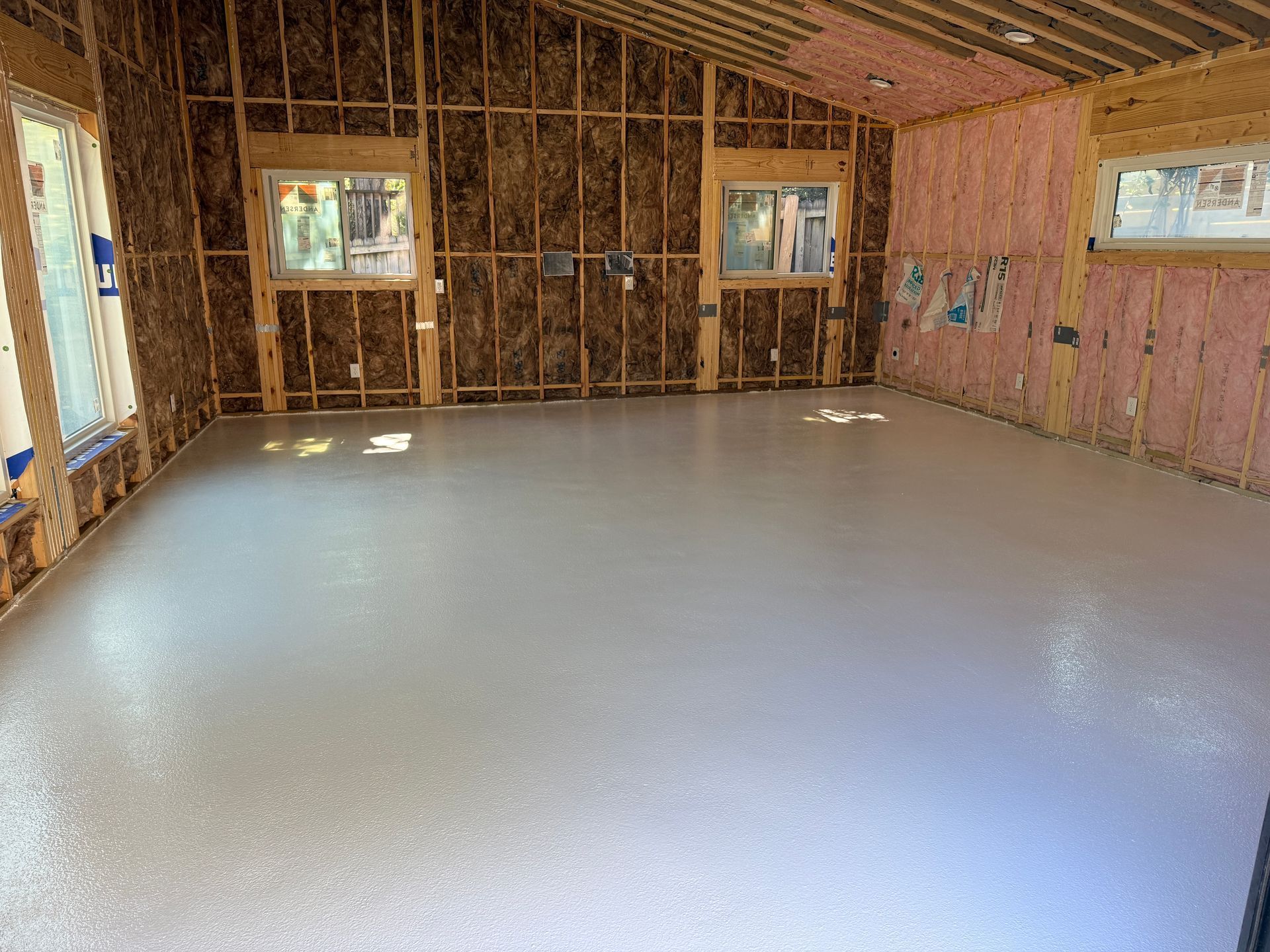 Unfinished room with exposed framing, pink insulation, and a smooth gray floor.